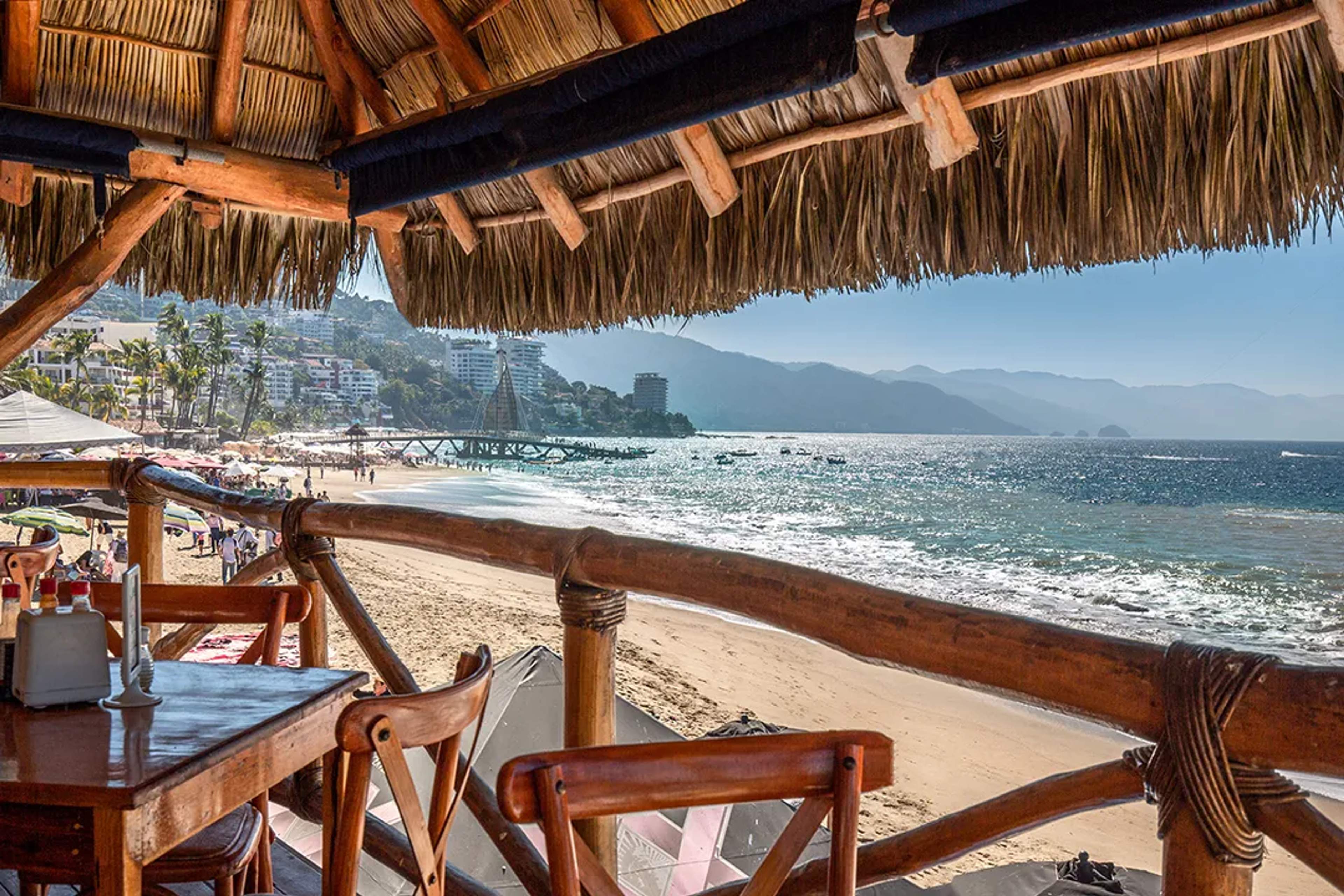 Beachfront restaurant in Puerto Vallarta with ocean views, wooden terrace seating, and the Sierra Madre in the background