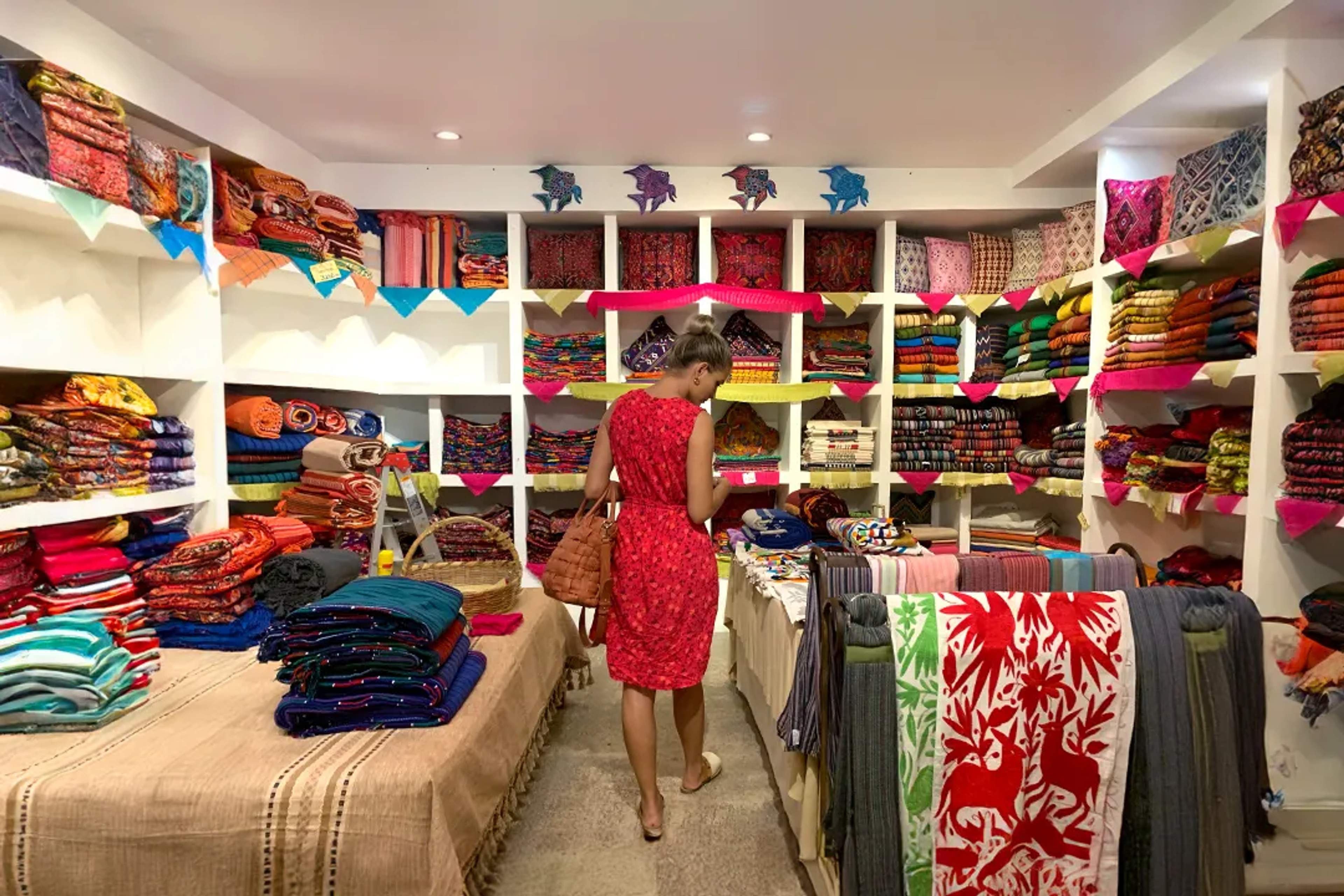 Woman shopping colorful handmade textiles in a cozy Mexican boutique full of vibrant fabrics.
