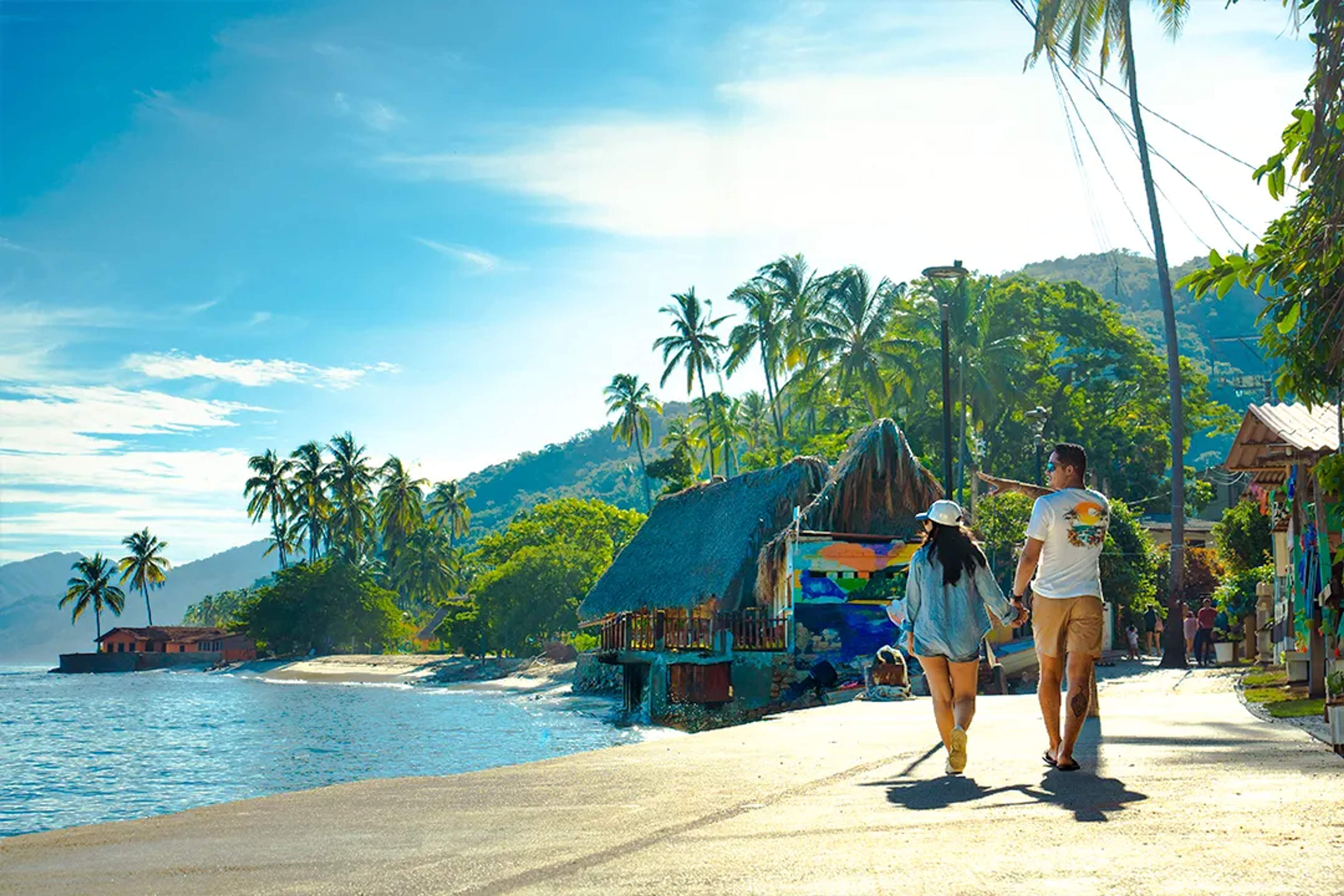 Couple walking along Yelapa beach village, palm trees, colorful huts and Sierra Madre coastline scenery