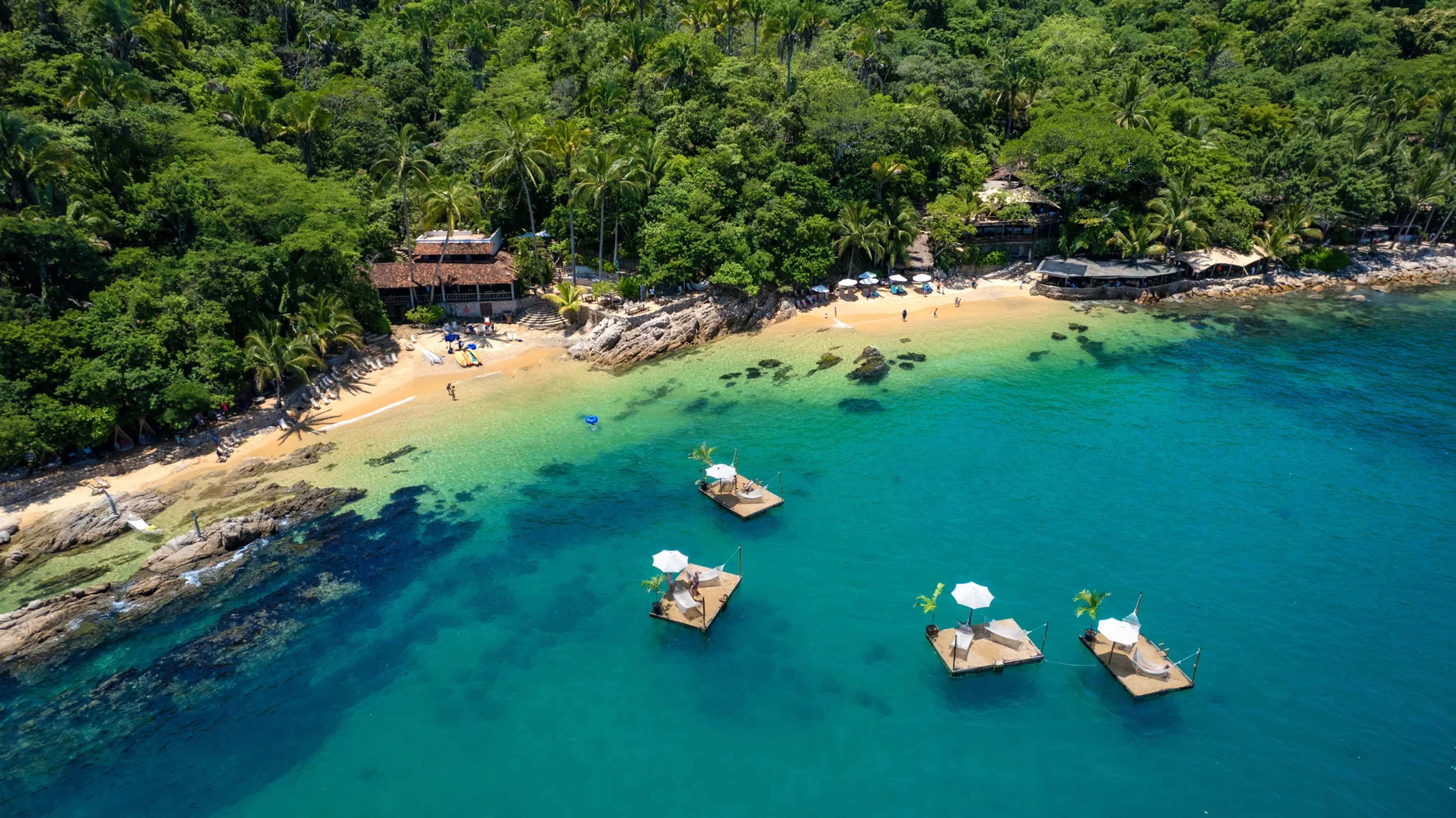 Vista aérea de la playa de Las Caletas con botes en aguas turquesas y selva exuberante enmarcando la orilla de arena dorada.