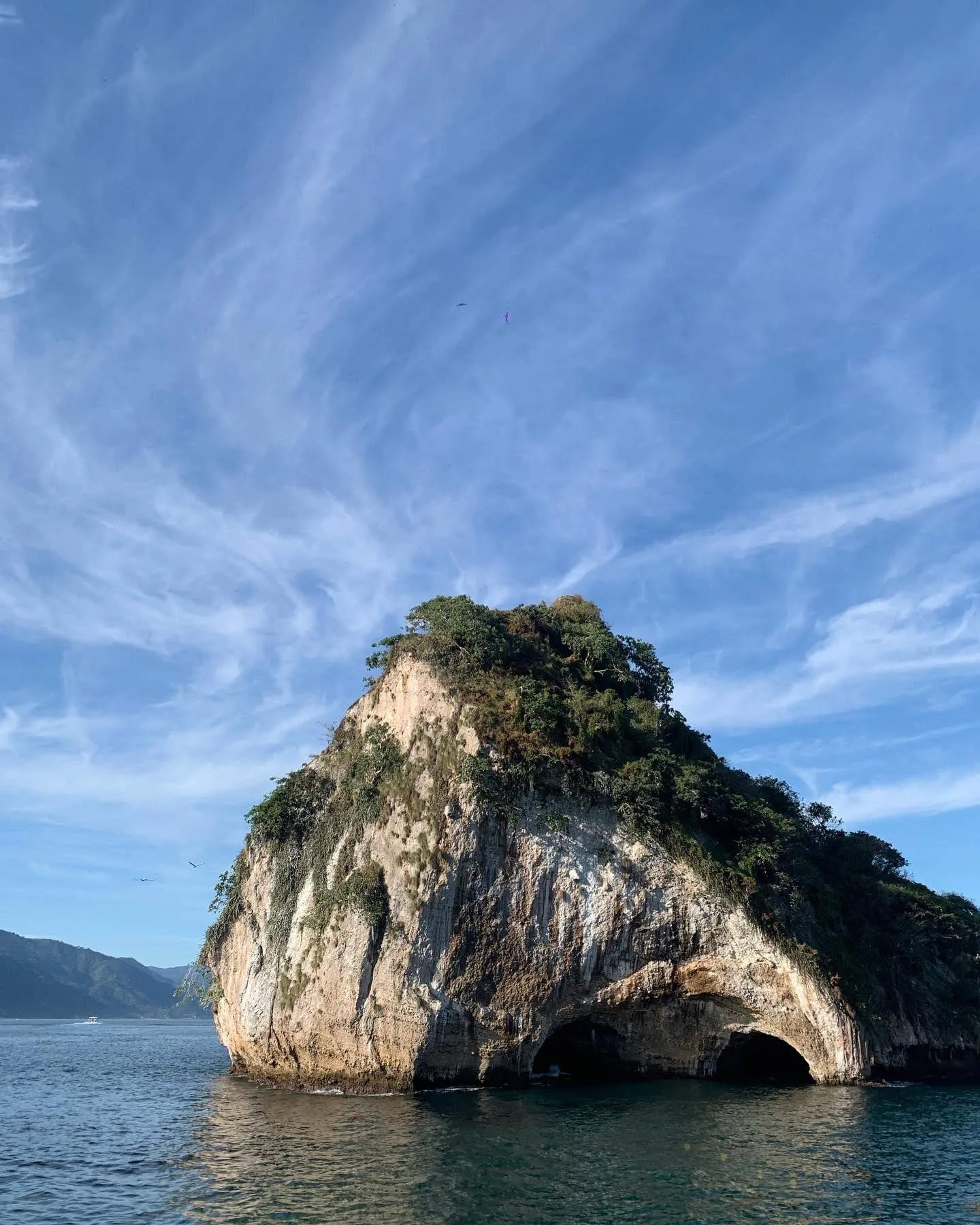 Formación rocosa de piedra caliza con una gran cueva arqueada emerge de aguas turquesas bajo un cielo despejado en Los Arcos.