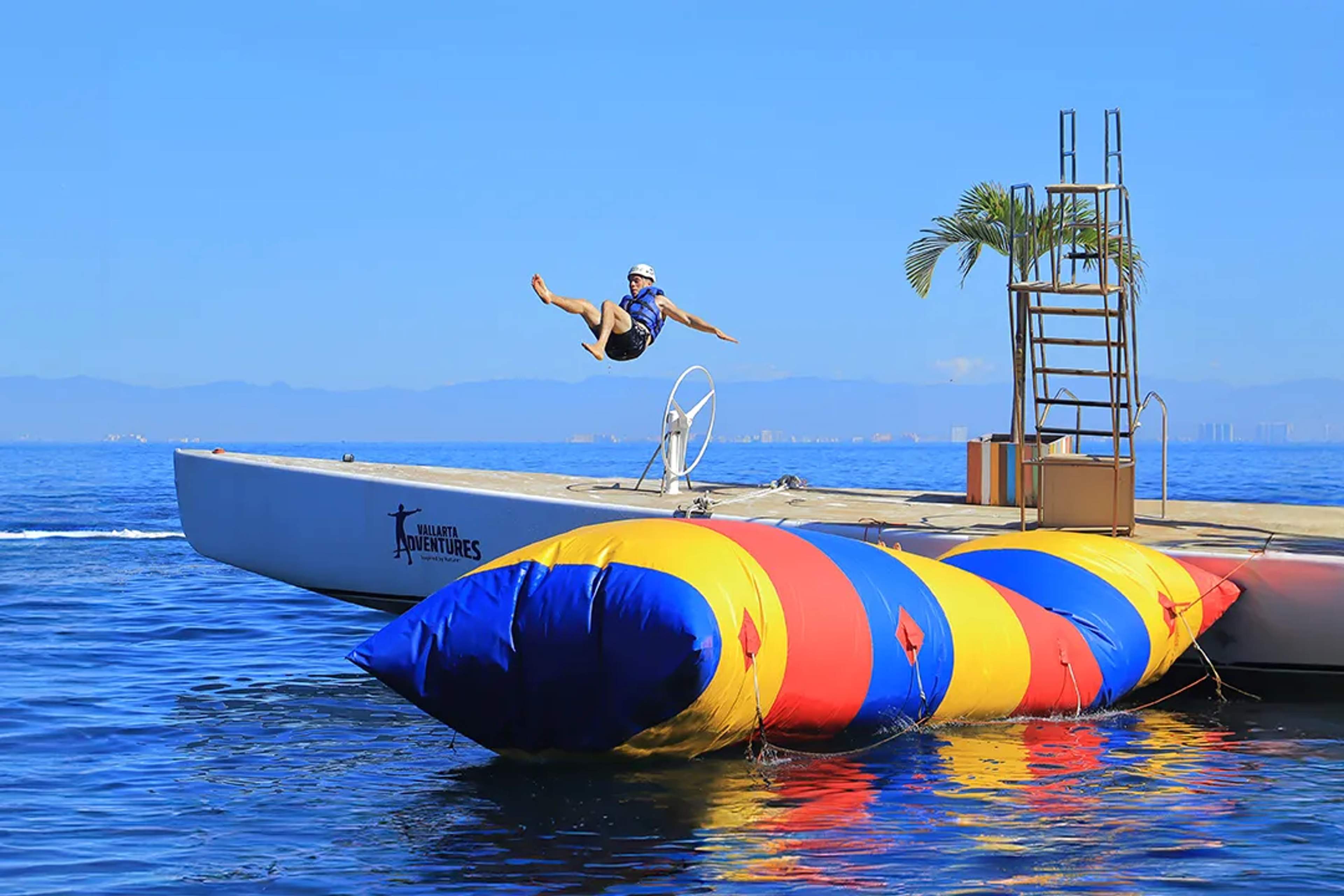 Person jumping from a colorful water blob during the Ocean Mania adventure tour in Puerto Vallarta