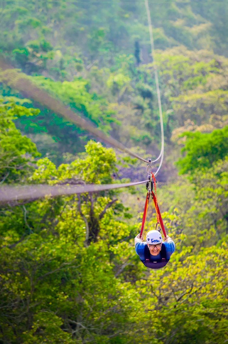Person ziplining over lush greenery on the Superman, the longest zipline in Puerto Vallarta, as part of Extreme Adventure.
