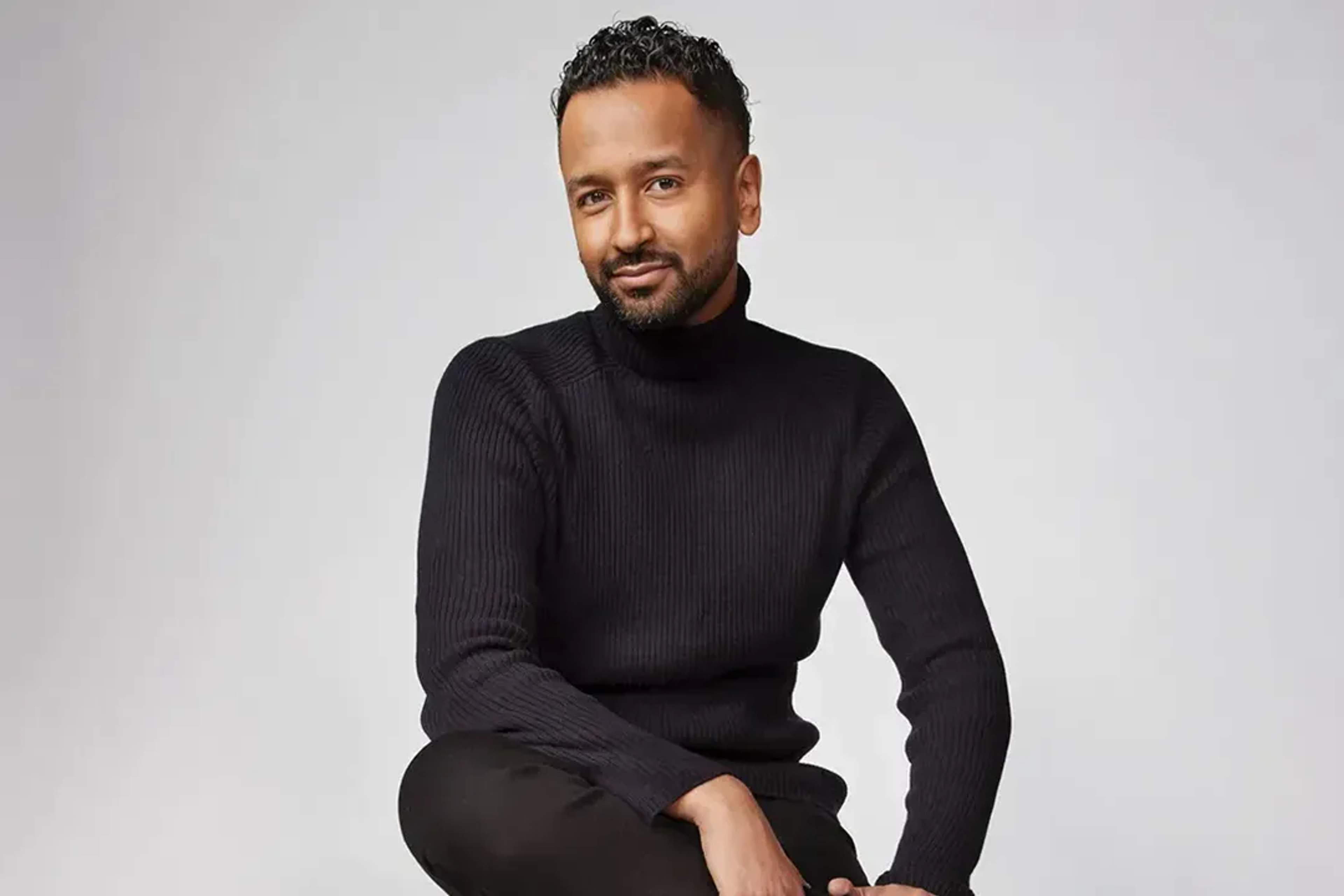 Portrait of Mukhtar Mukhtar, dressed in black, seated with elegance and confidence.