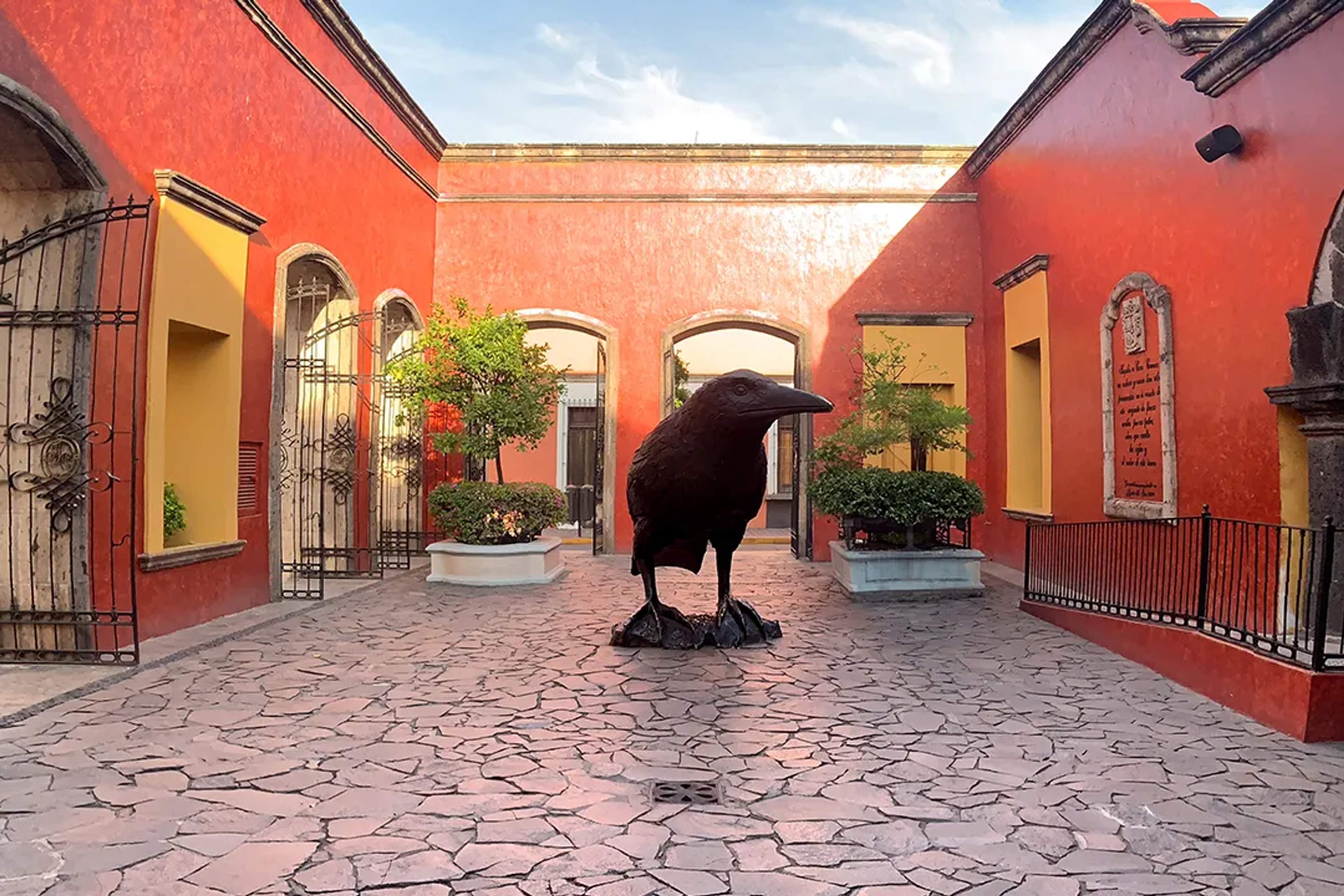 Patio de la Hacienda La Rojeña con muros rojos, árboles y una gran escultura de cuervo al centro.