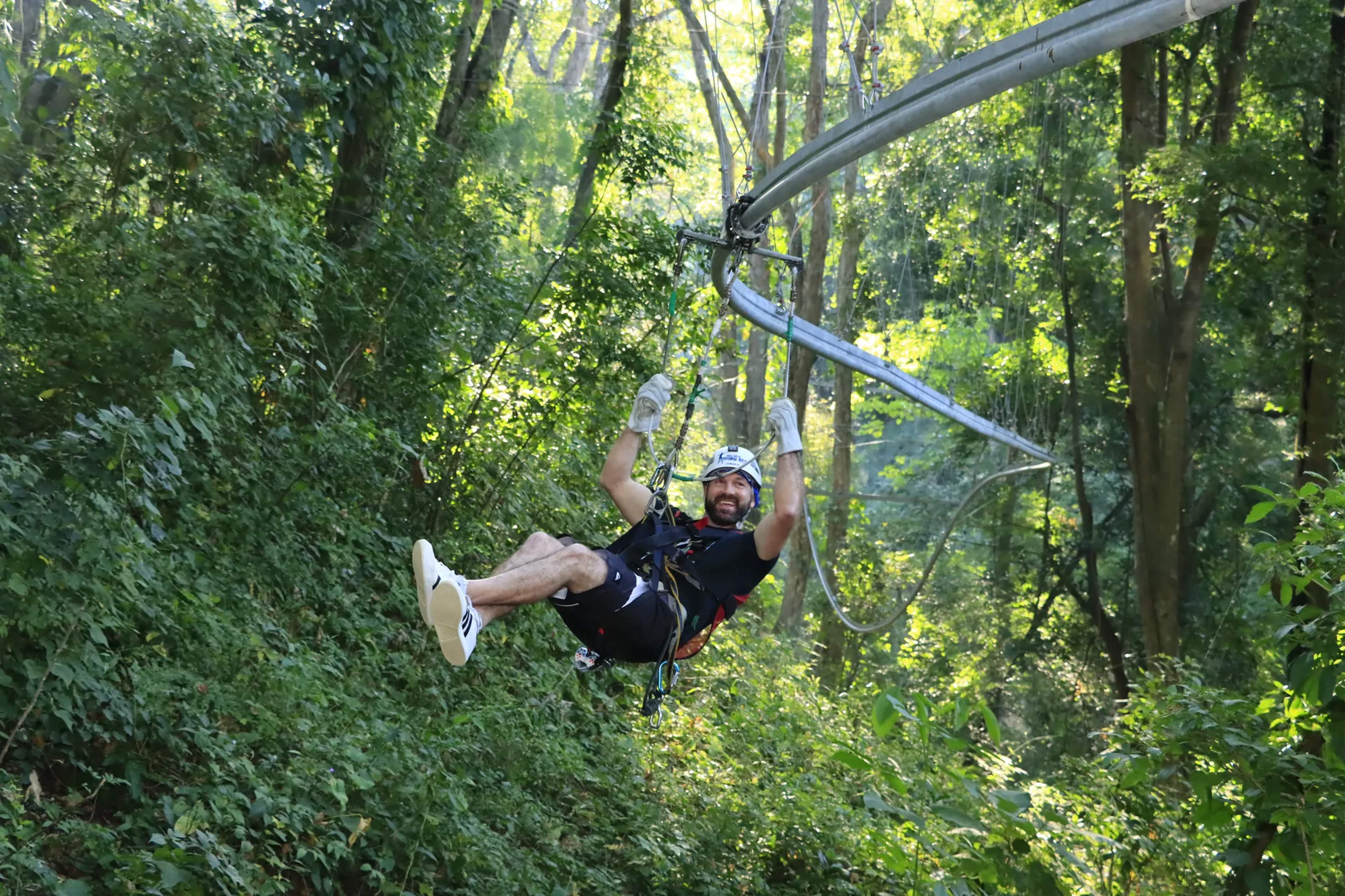 A zipliner in full safety gear descends a blue zipline cable through a dense Mexican jungle canopy.