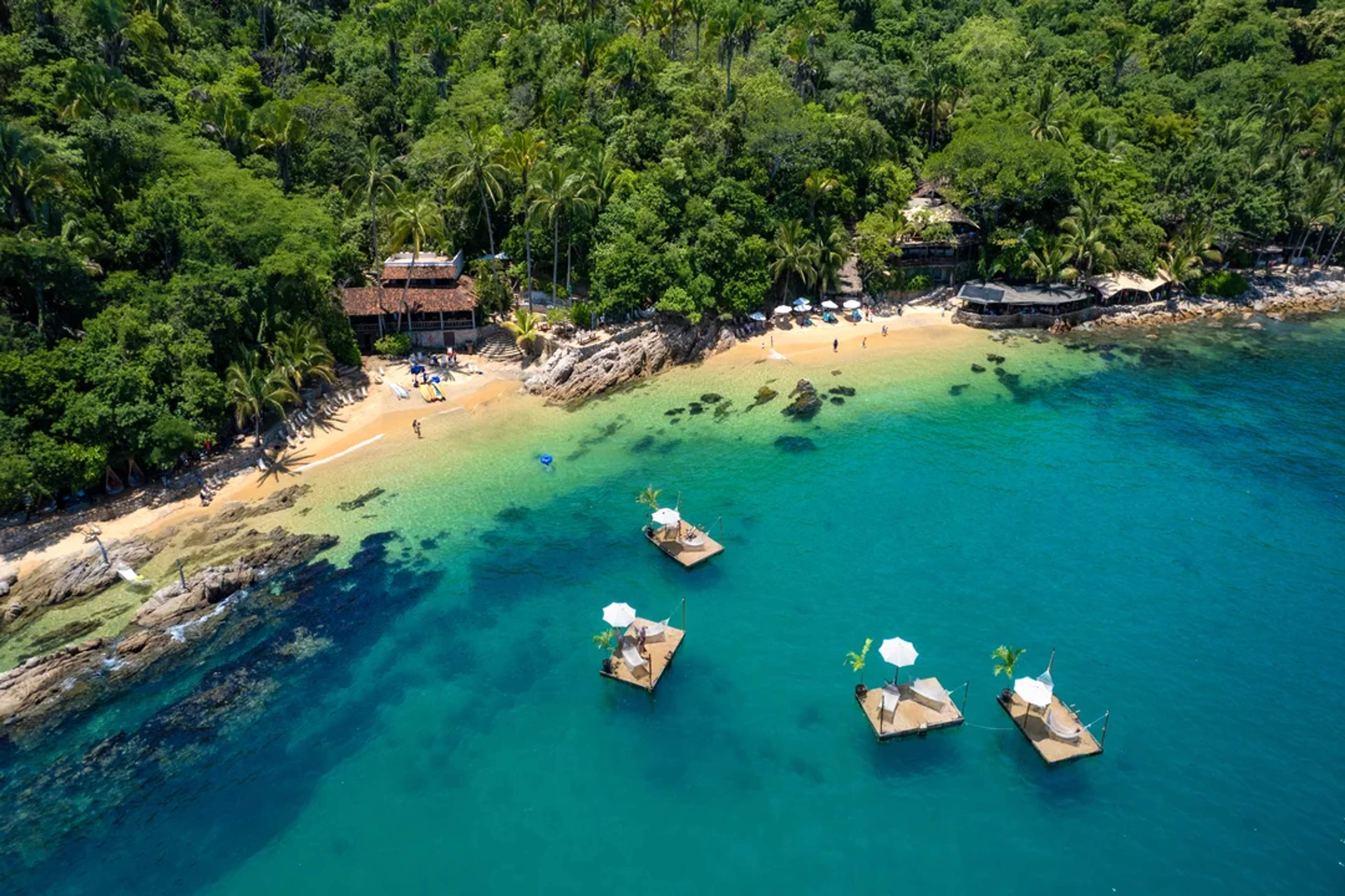 Playa tropical con camastros flotantes, agua turquesa cristalina y selva exuberante.