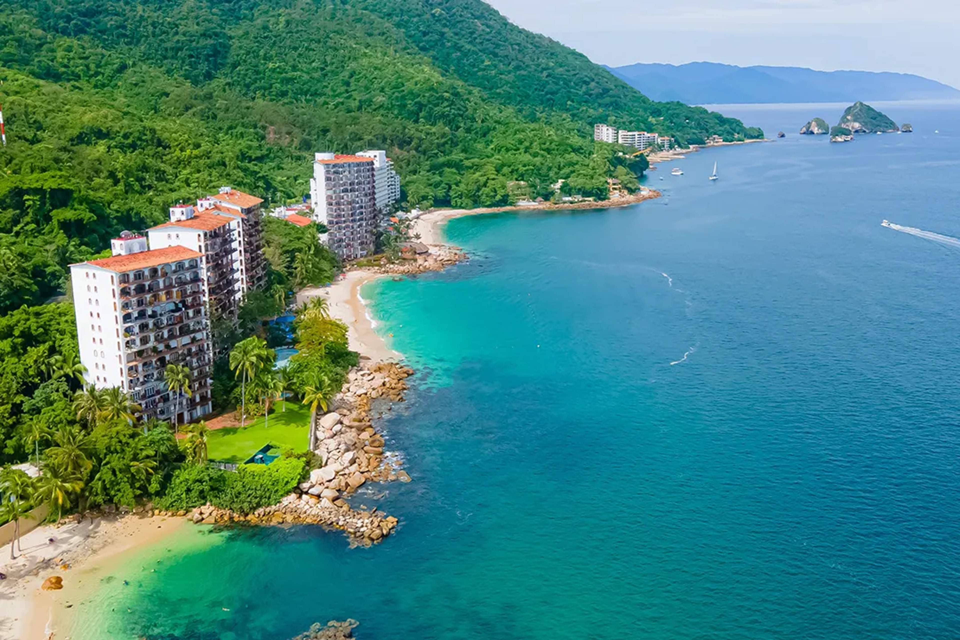 Tropical beach with turquoise water, lush jungle, and beachfront buildings of Puerto Vallarta.