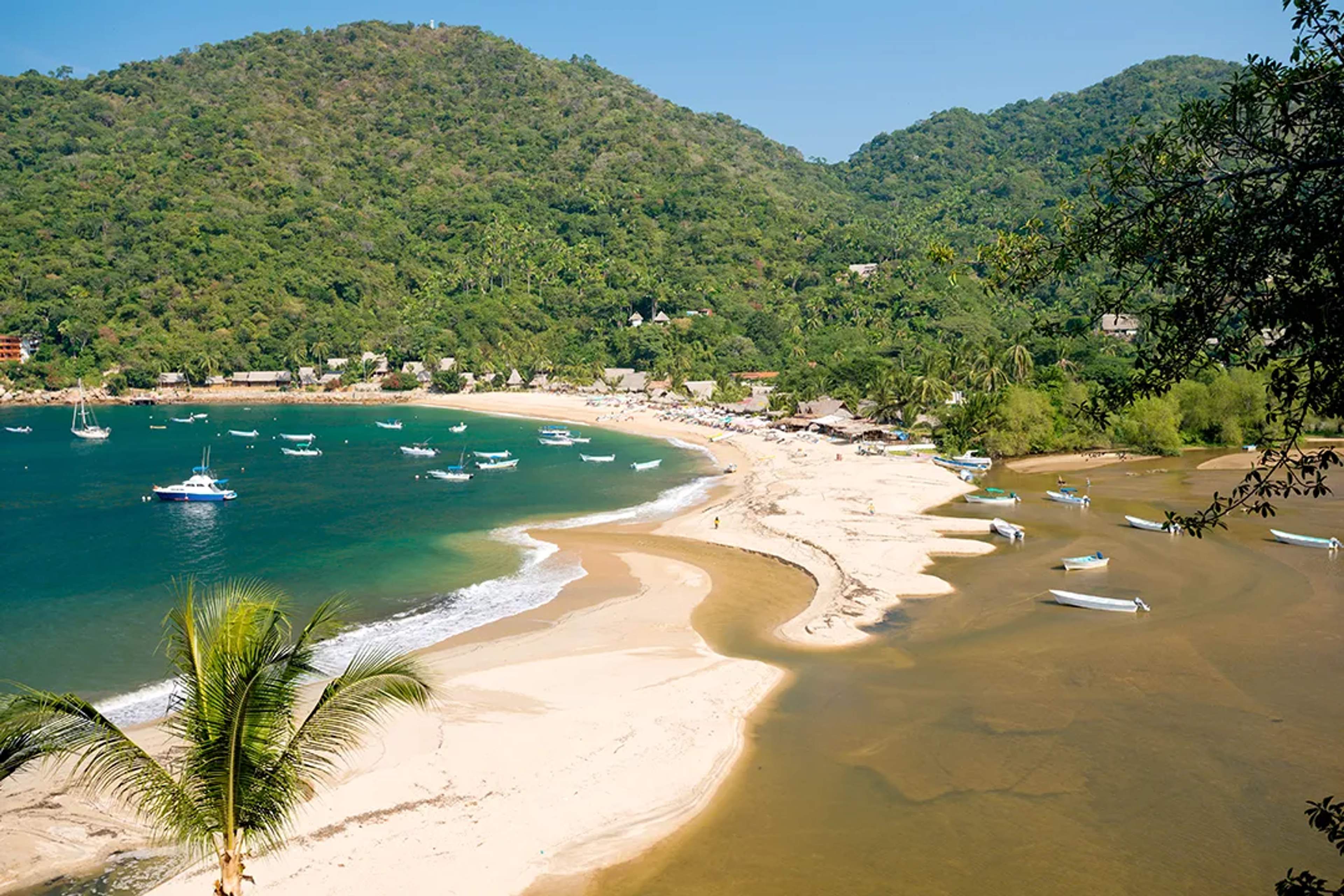 Lanchas flotan en la bahía turquesa de Yelapa, rodeada de selva y arena dorada.
