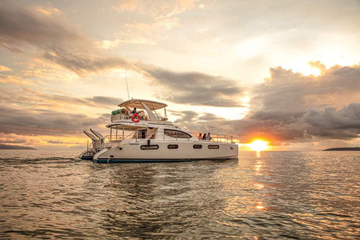 A yacht cruising at sunset on the ocean, with dramatic clouds and golden light reflecting on the water.