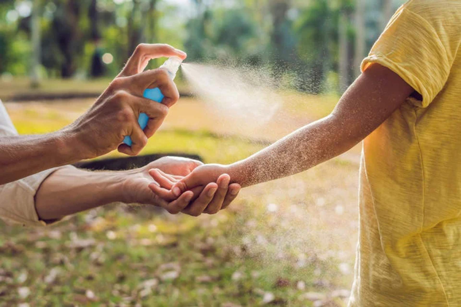 An adult spraying bug spray on a child's arm outdoors to protect from insects.
