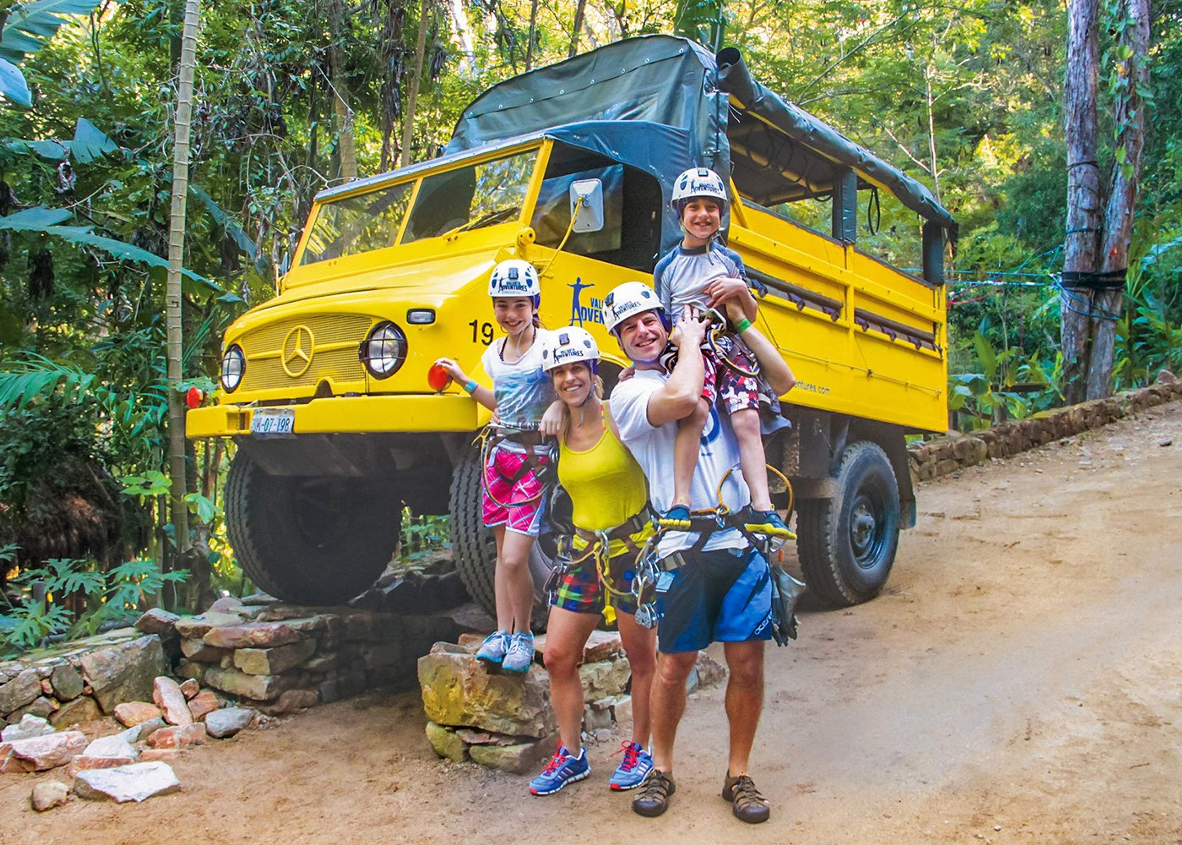 A family ready for an outdoor adventure, posing in front of a yellow Unimog vehicle at Vallarta Adventures.