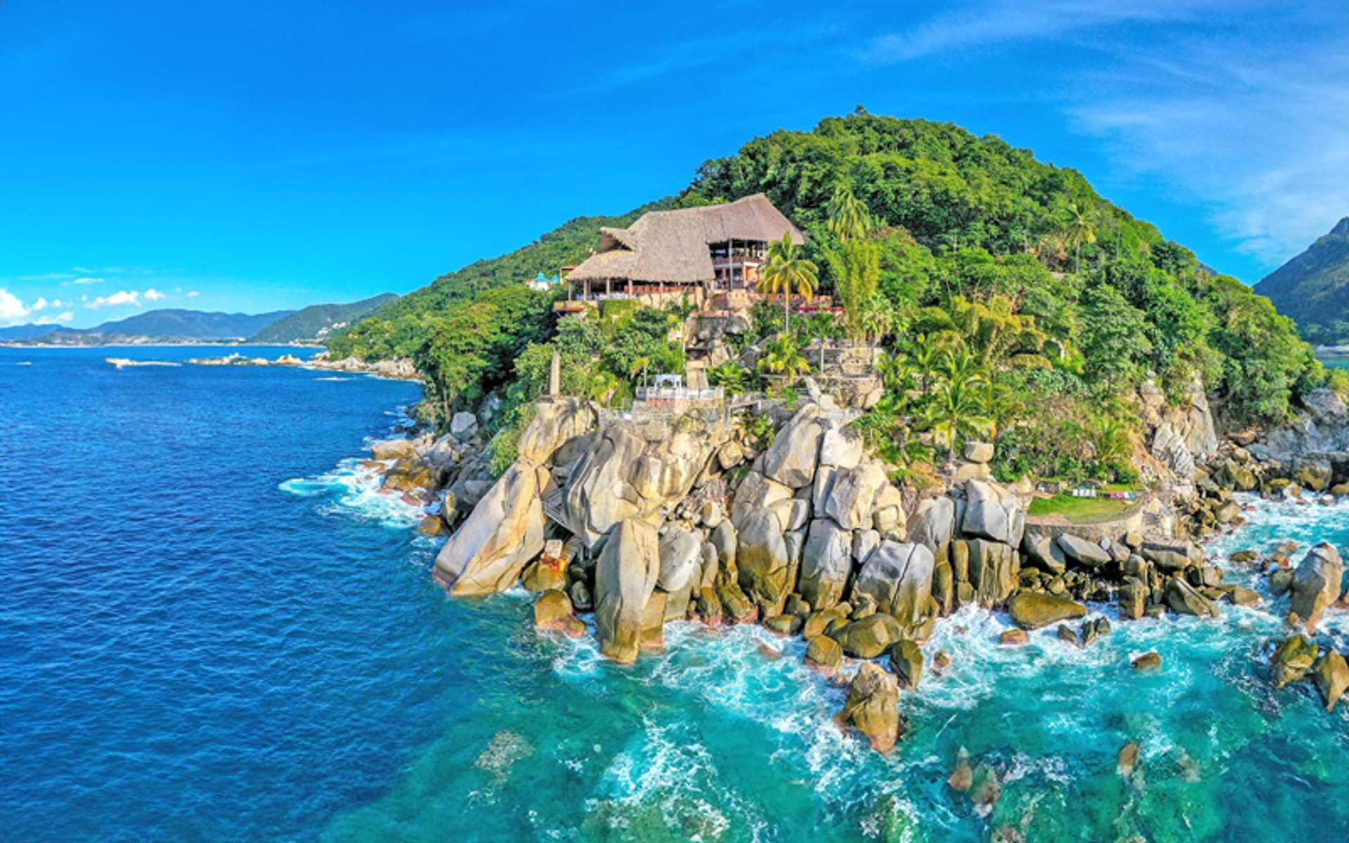 A stunning coastal view of a cliffside restaurant surrounded by lush greenery, overlooking the vibrant blue ocean.