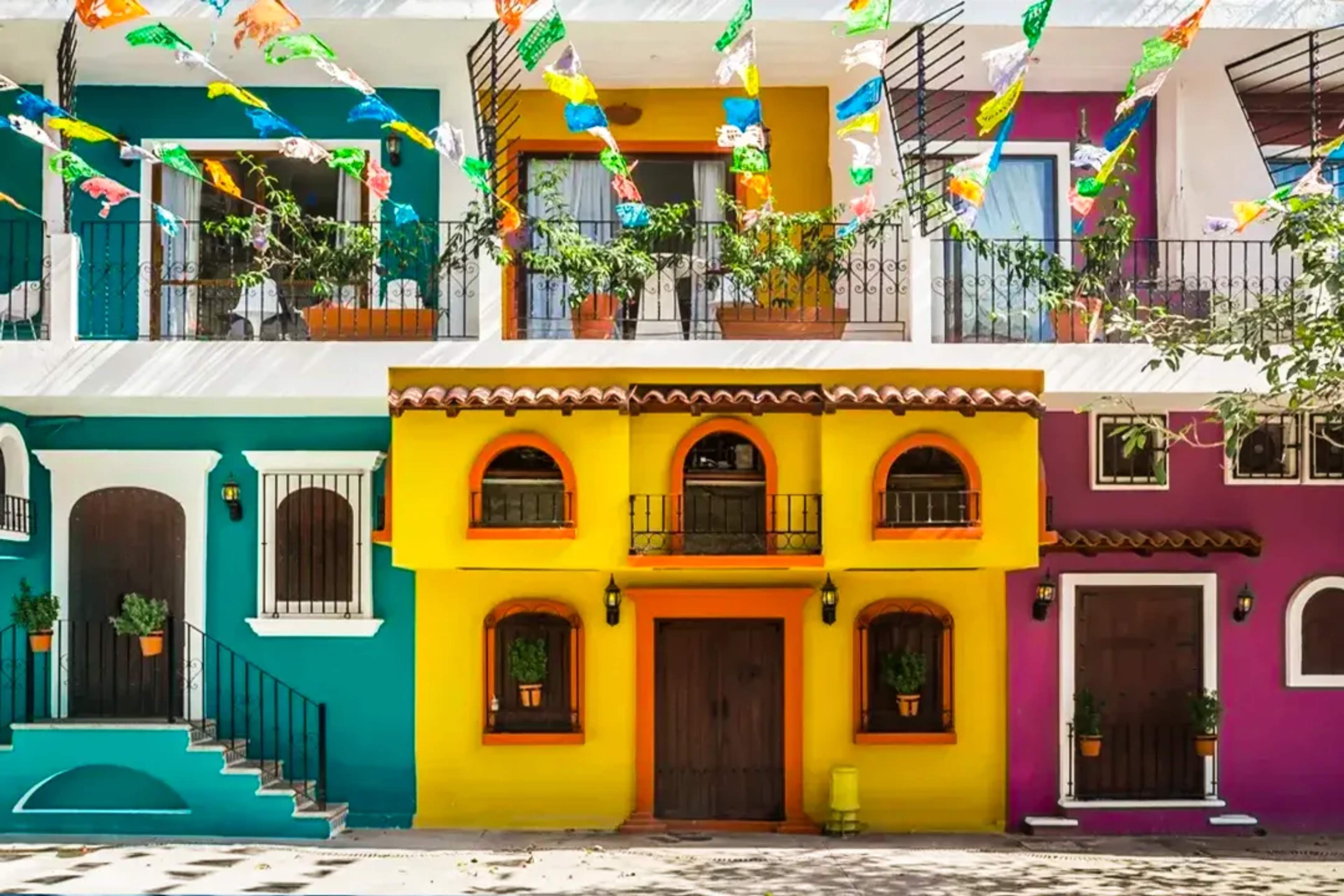 A vibrant street view with colorful Mexican-style houses, papel picado, and charming balconies.