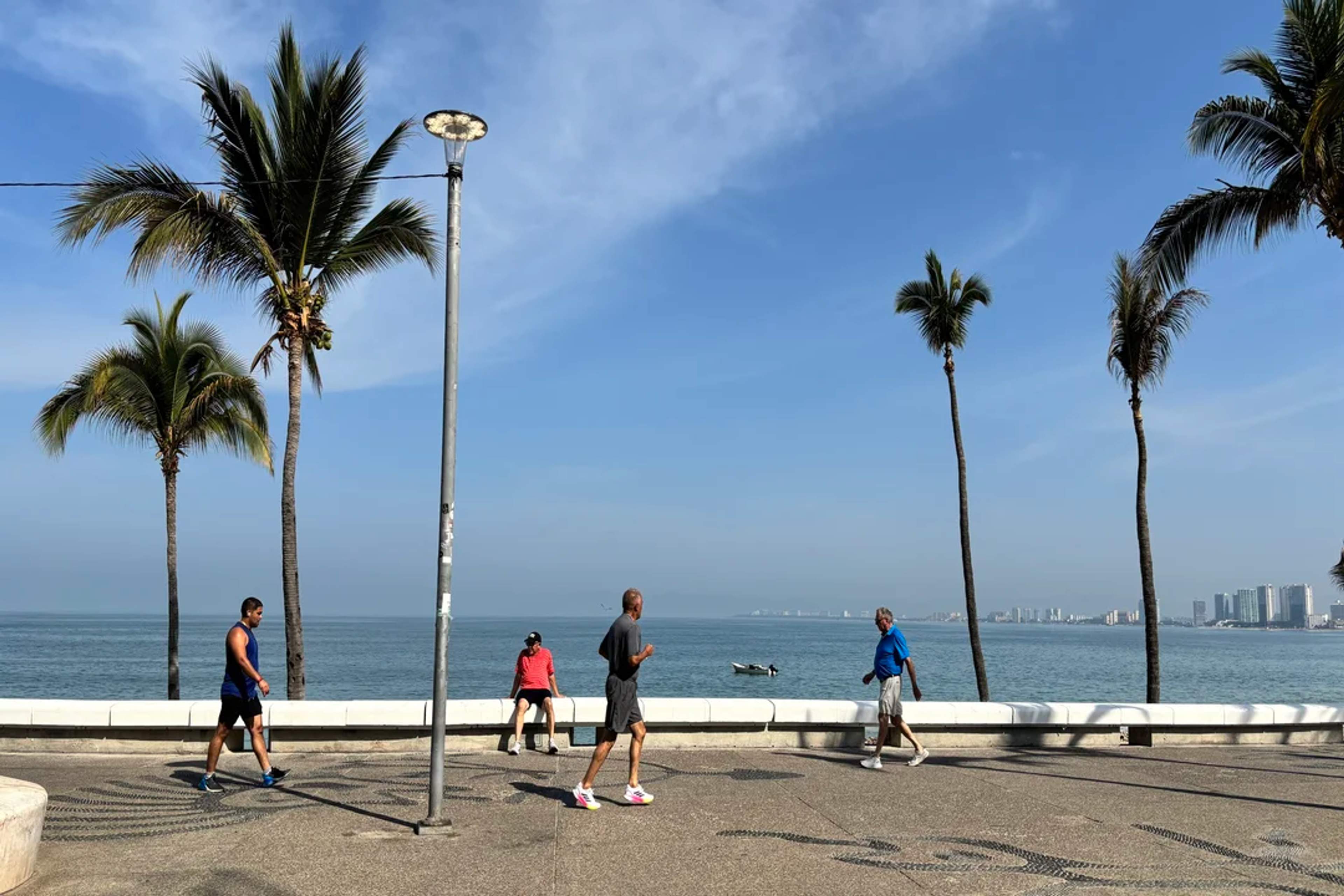People jogging and walking by the ocean on a sunny morning at the Puerto Vallarta Malecón.