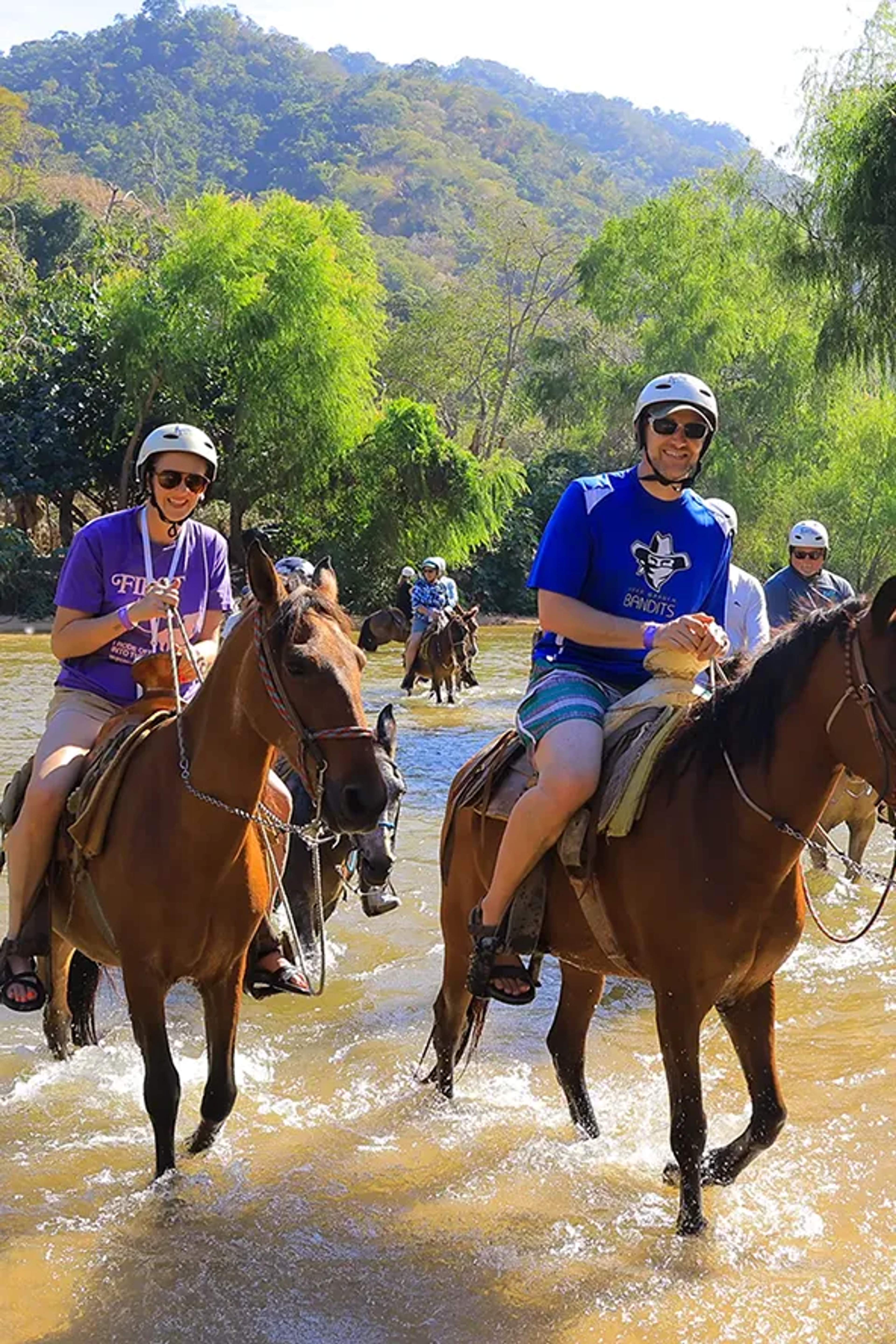 Tour a caballo cruzando un río rodeado de exuberante vegetación tropical en Puerto Vallarta.