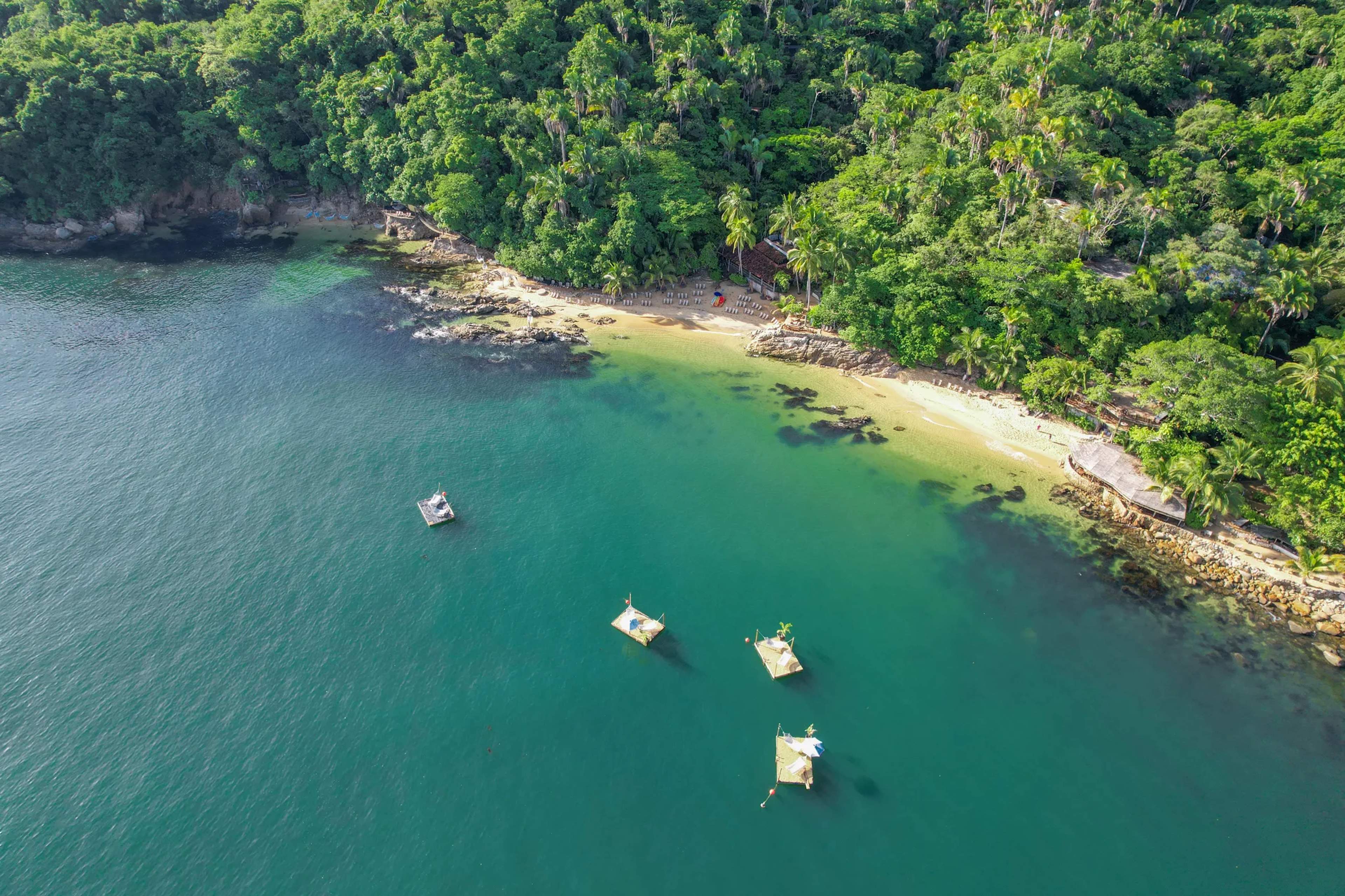 Vista aérea de la cala secreta Las Caletas con aguas turquesas, botes anclados y frondosa selva que rodea la playa.