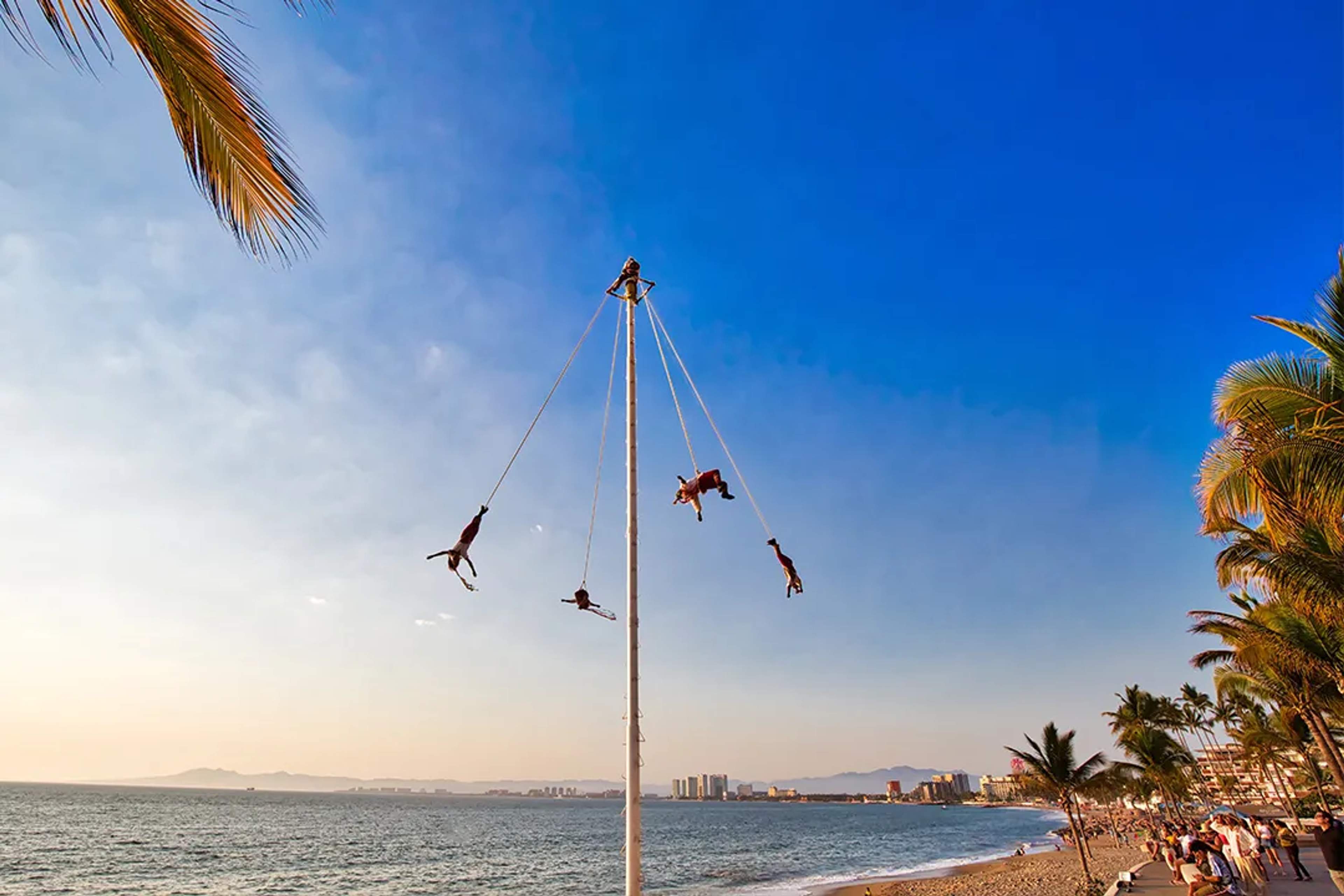 Traditional Voladores de Papantla flying over Puerto Vallarta’s beach at sunset.