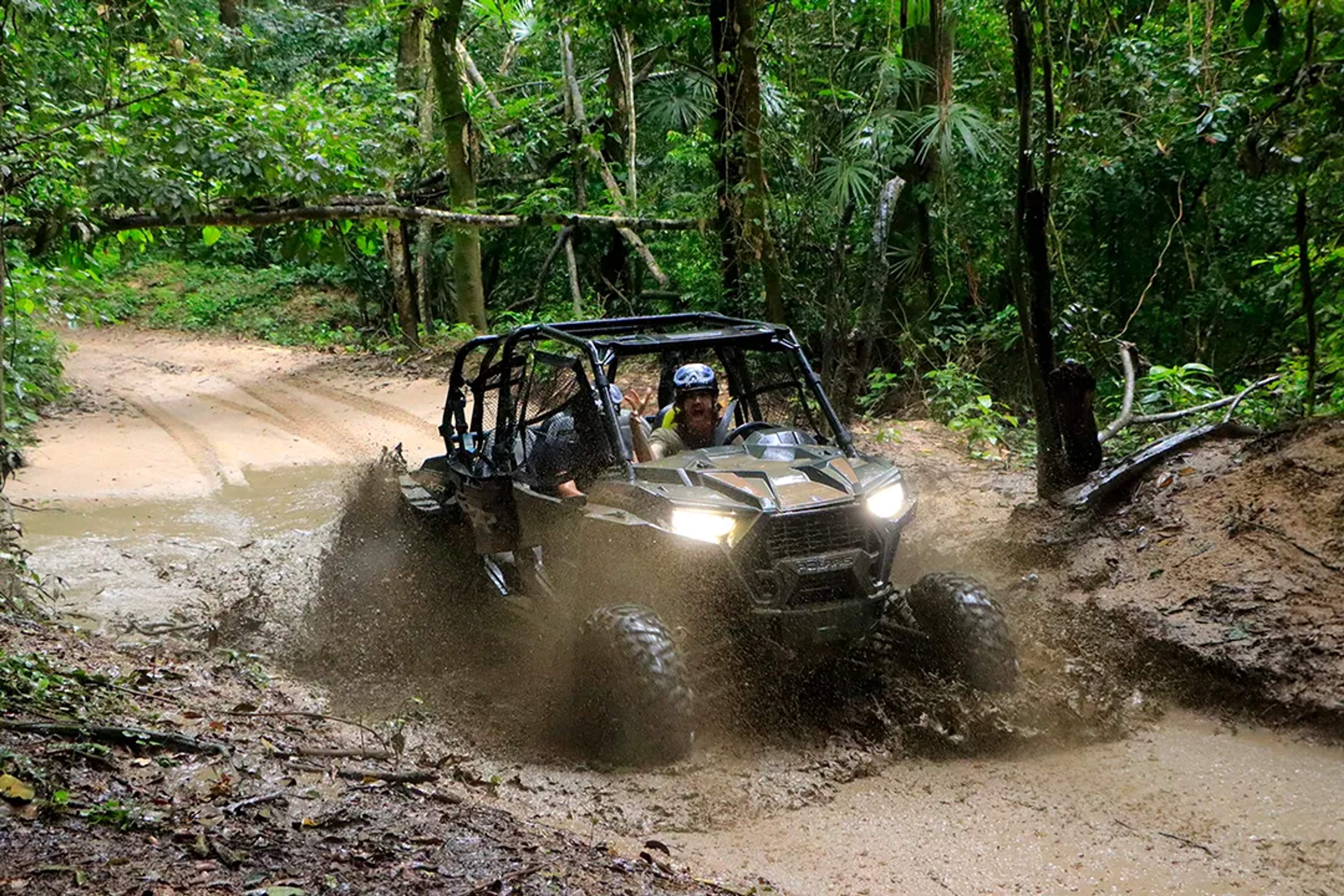 Vehículo todoterreno cruzando lodo en un camino selvático durante una aventura llena de adrenalina.