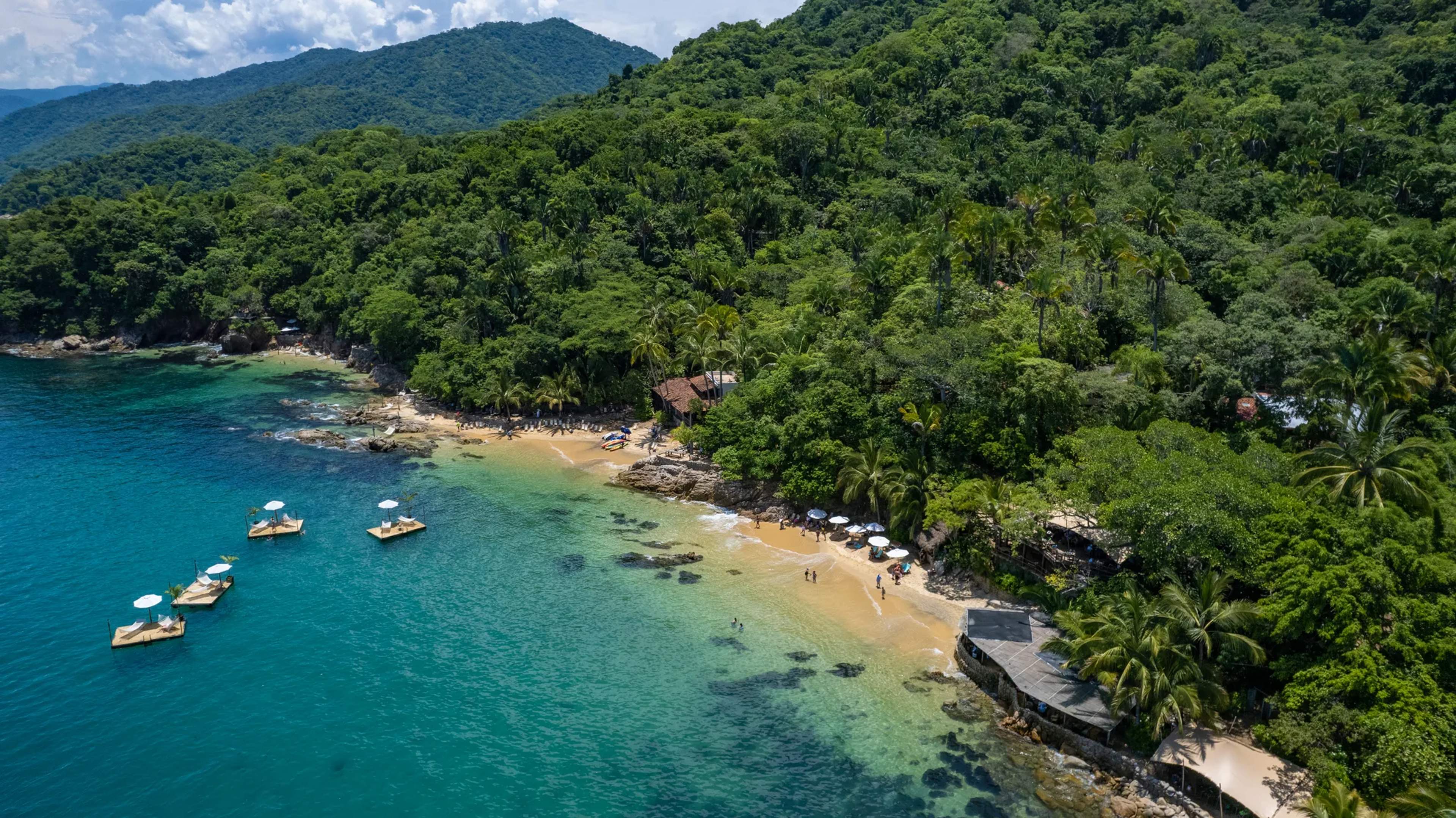 Vista aérea de la ensenada Las Caletas con aguas turquesas, botes anclados y selva tropical que llega a la orilla de arena.