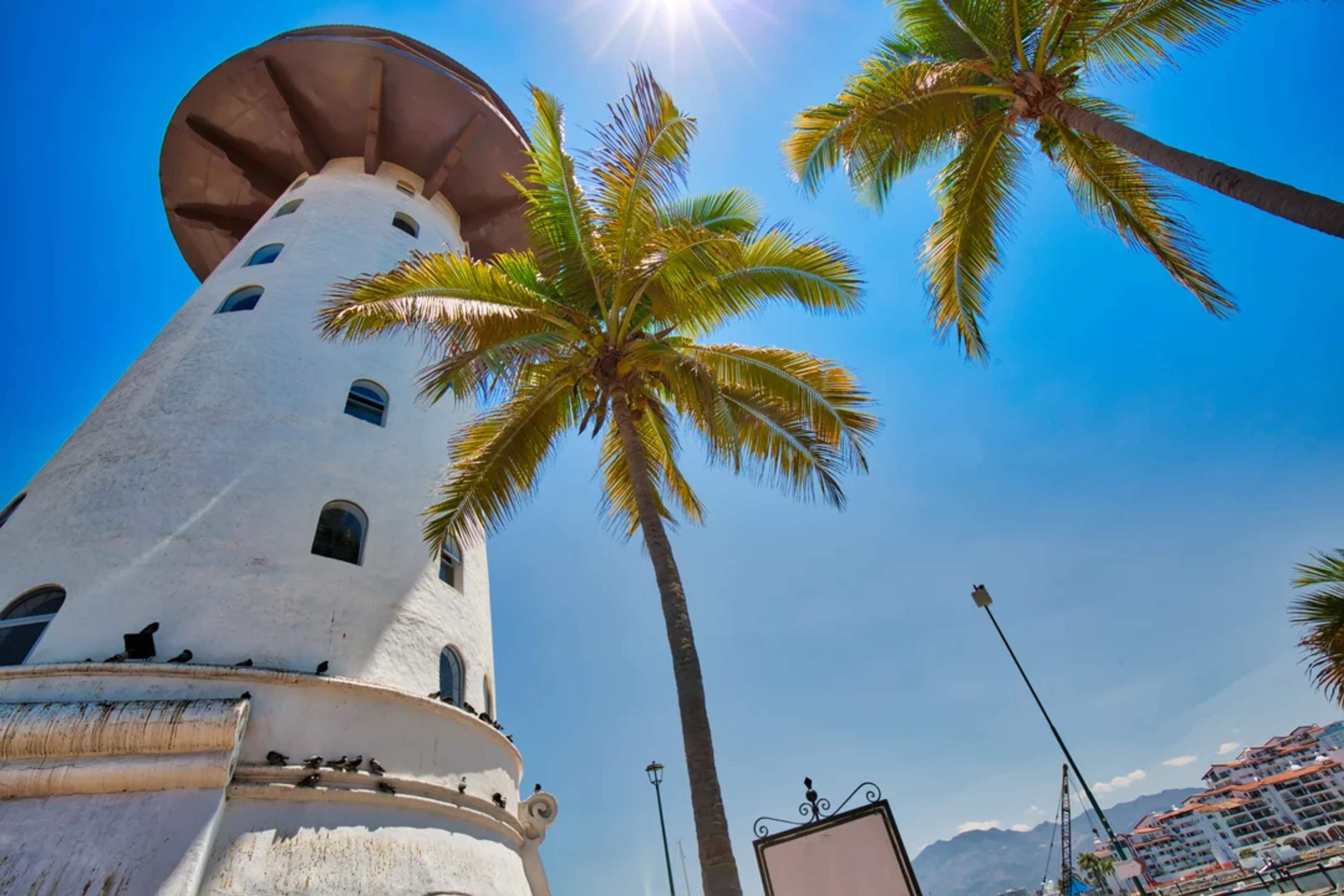 Faro blanco y palmeras bajo el sol brillante en la Marina de Puerto Vallarta, Jalisco.