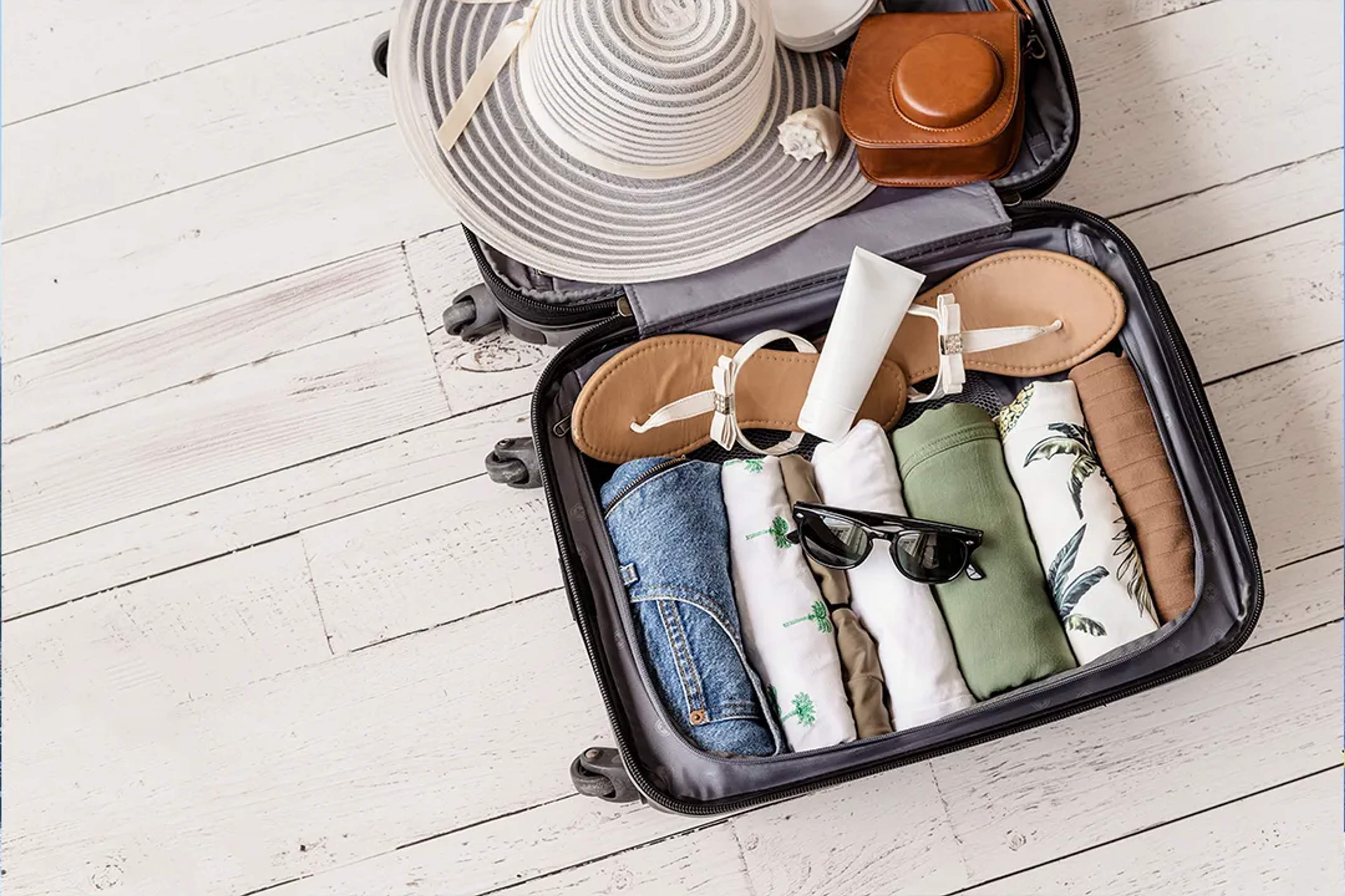 Open suitcase with summer clothes, hat, sandals and travel essentials for a beach vacation packing guide