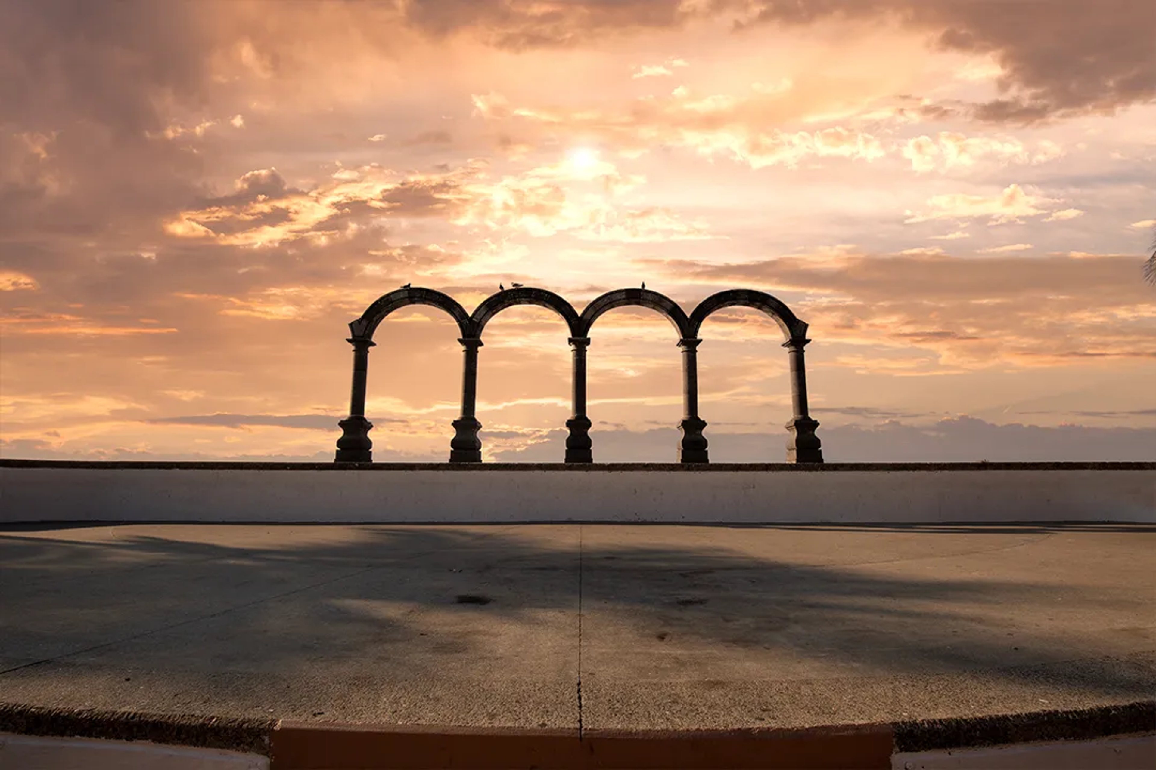 Iconic arches on the Malecón at sunset, casting long shadows under a golden sky.