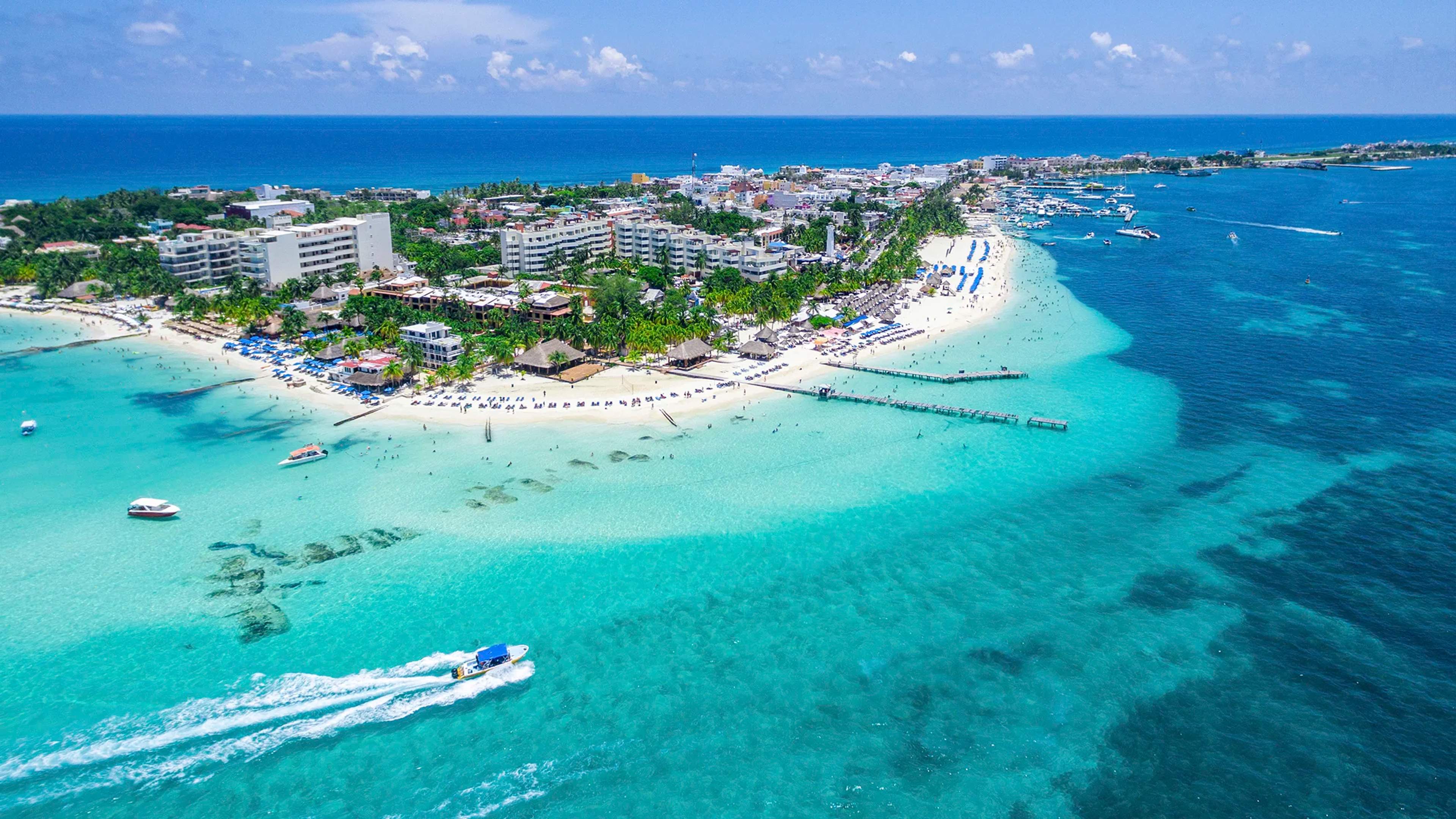 Aerial view of Isla Mujeres with white sandy beaches, turquoise waters, and boats cruising the coast.