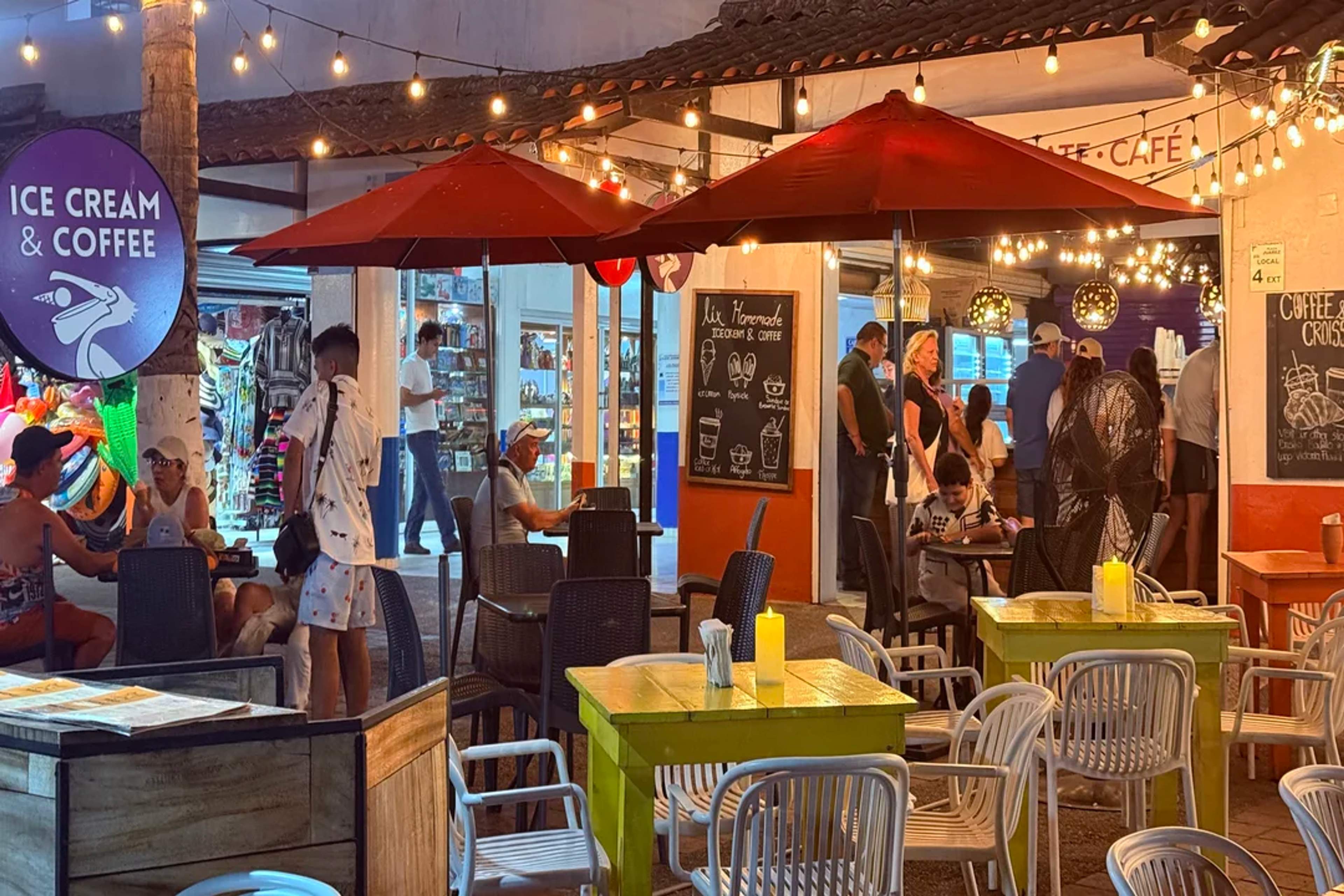 Cozy ice cream café with colorful tables, string lights, and people enjoying a warm evening.