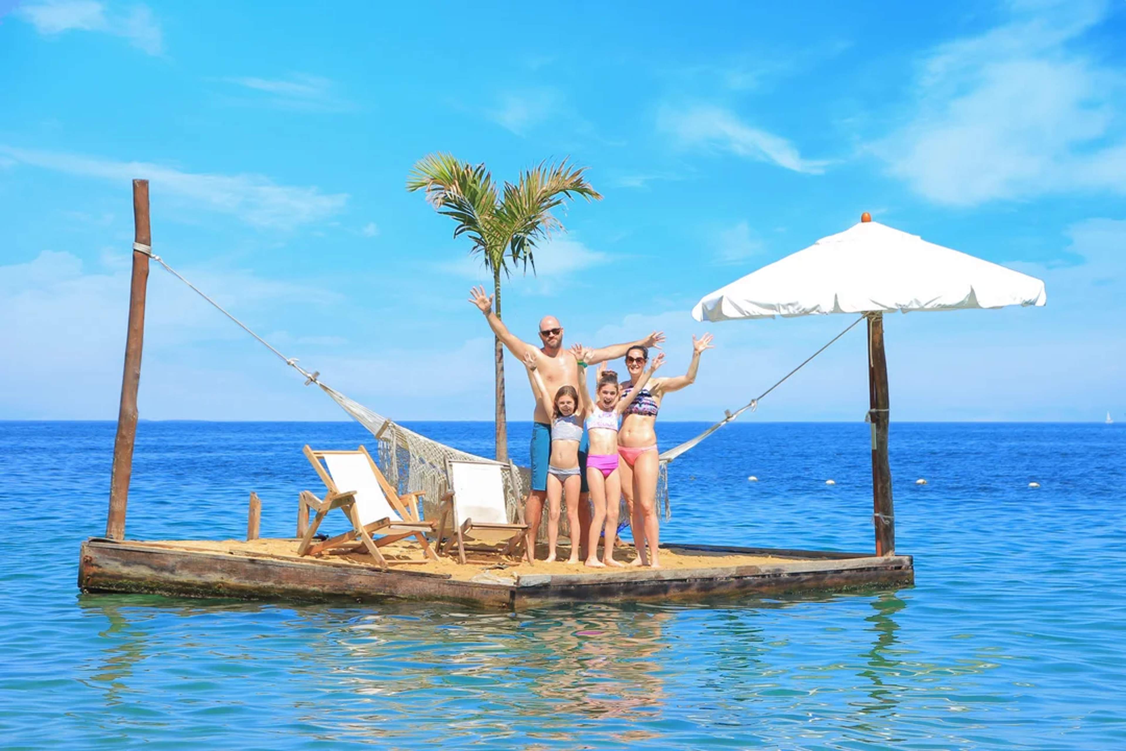 Happy family waves from a floating island with chairs, umbrella, and hammock in the ocean at Las Caletas.