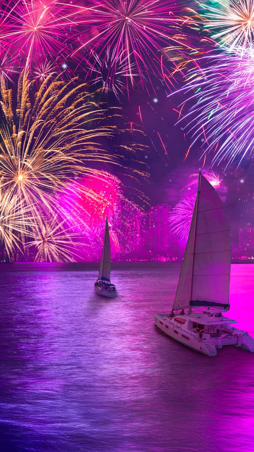 Sailboats glide under dazzling purple fireworks, lighting the city skyline and ocean waters.