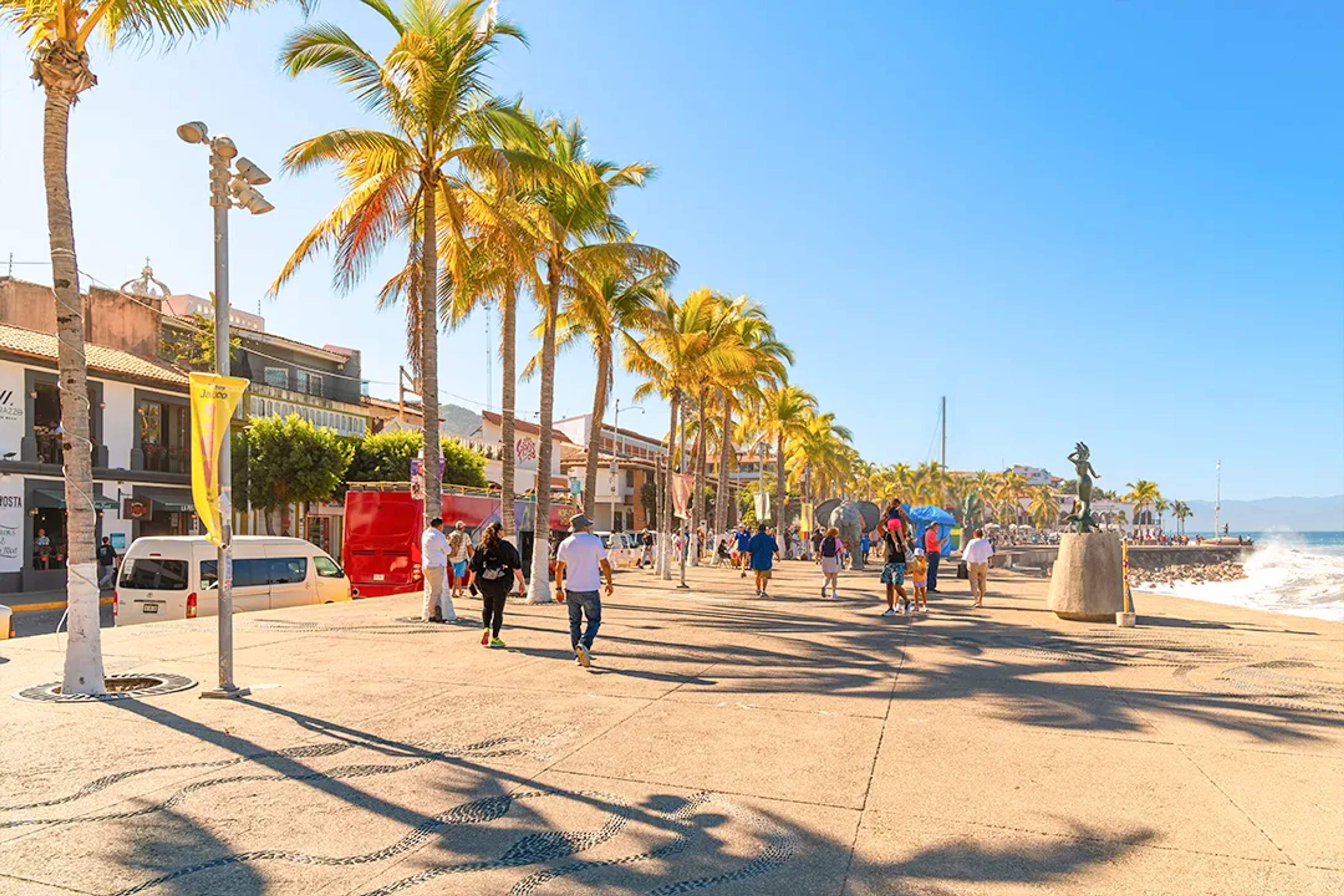 Walk along the Puerto Vallarta Malecón on a guided city tour, featuring ocean views, palm trees, art and local life.