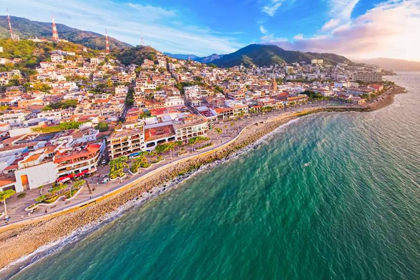Estatua frente al mar y vista urbana en el Malecón de Vallarta bajo un cielo soleado.