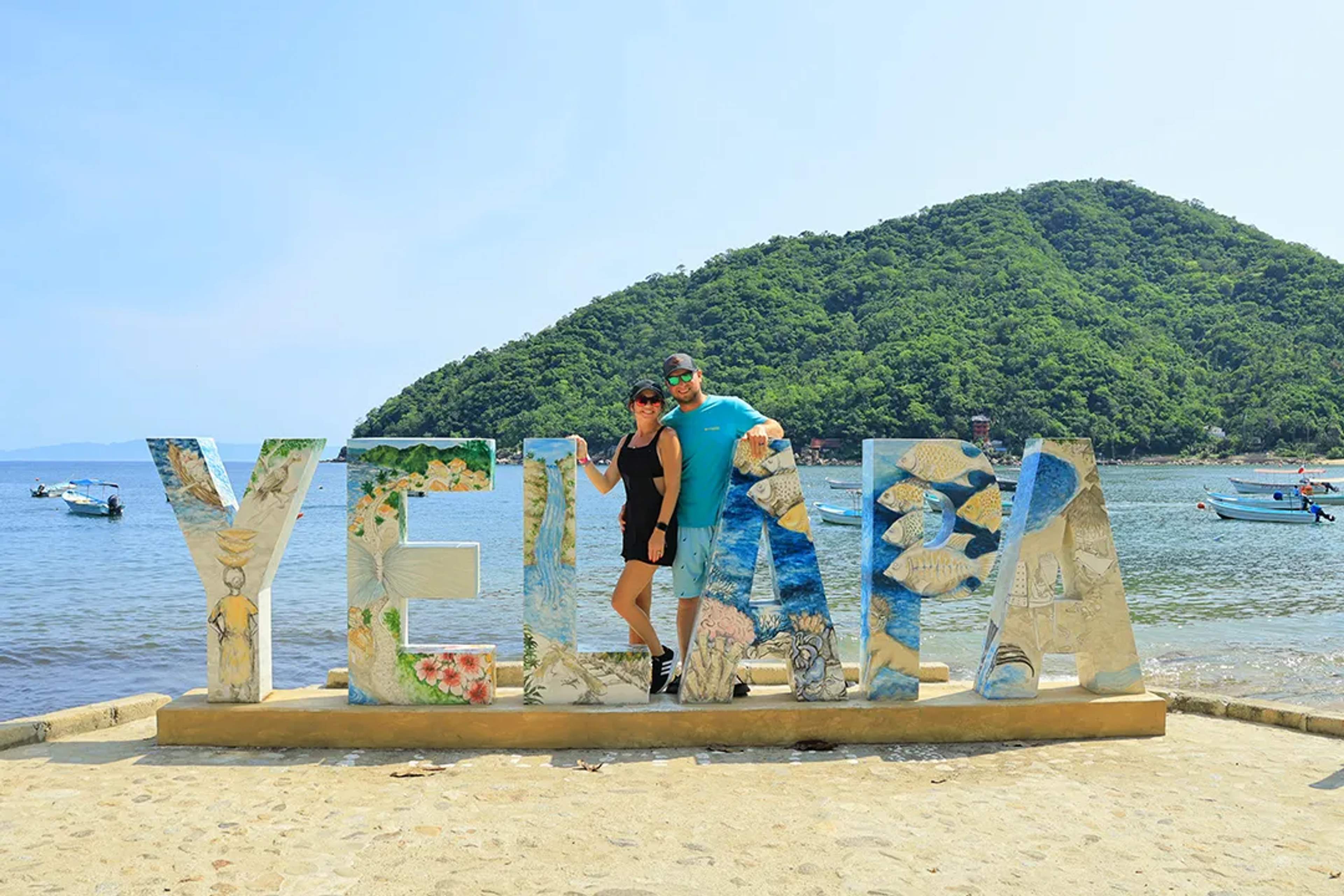 Pareja en el letrero de Yelapa durante el tour Yelapa y Majahuitas de Vallarta Adventures en la playa