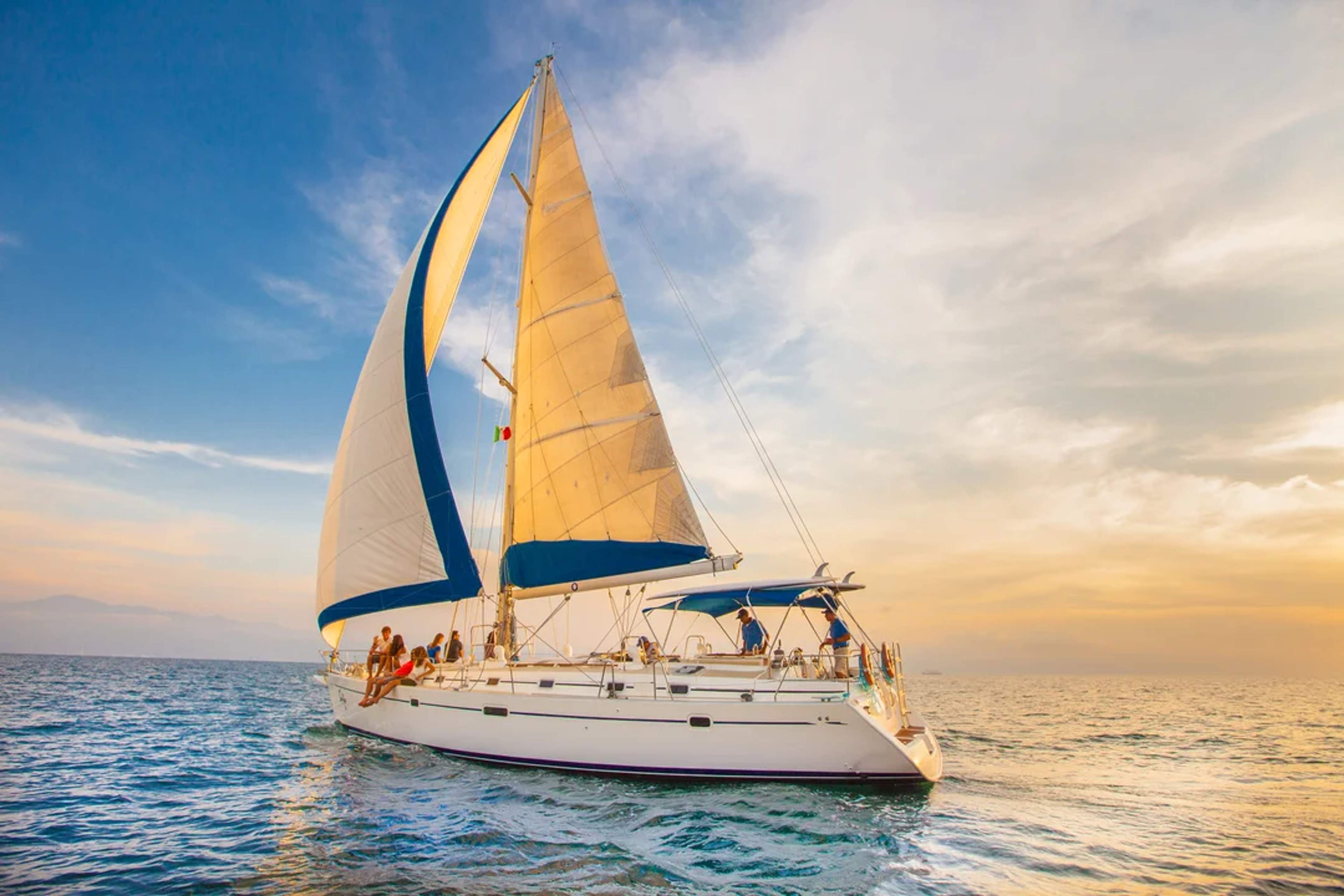 Velero navega al atardecer con pasajeros disfrutando del mar y el cielo dorado de Cabo.