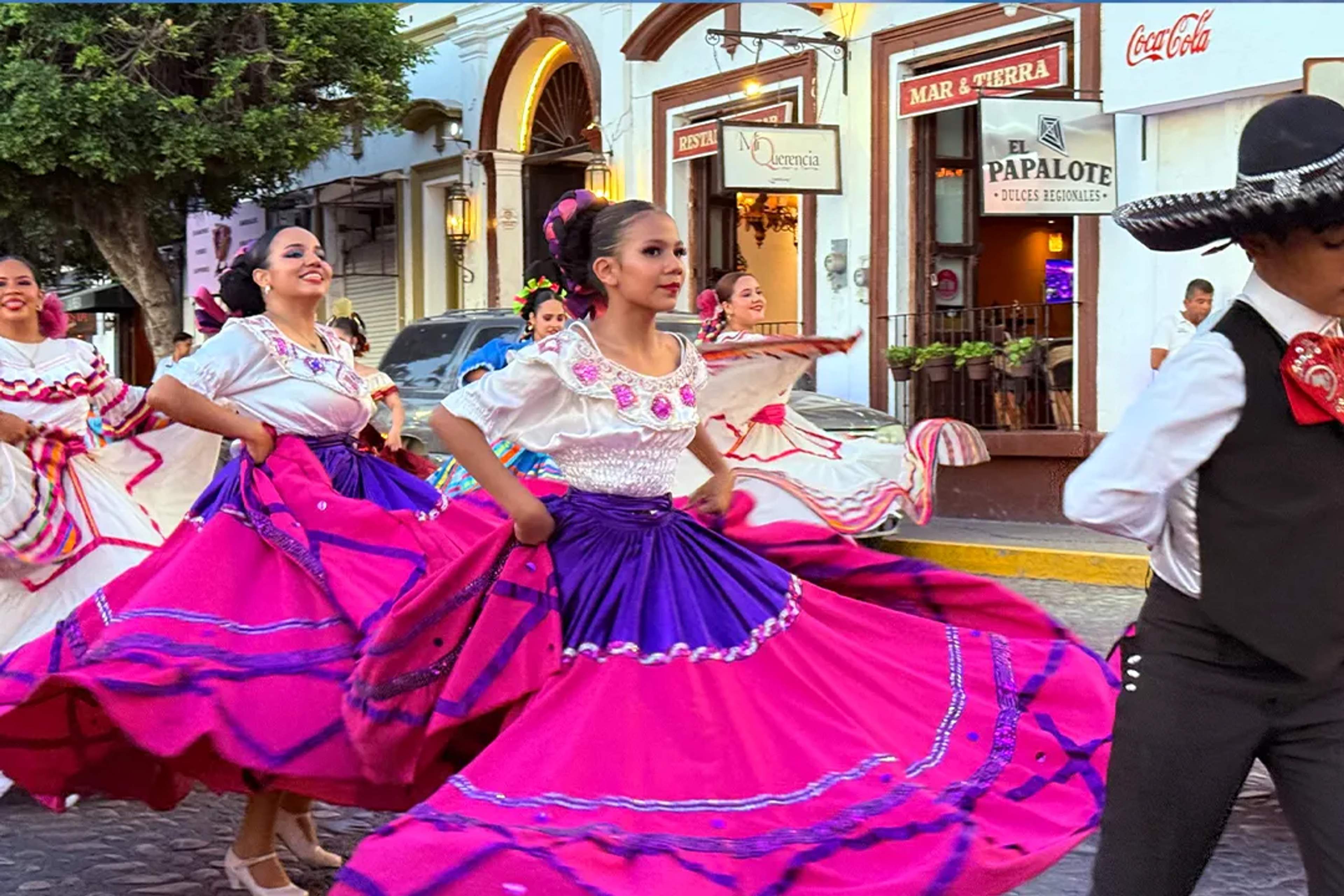 Bailarinas con vestidos típicos mexicanos bailan folclor en una calle empedrada.