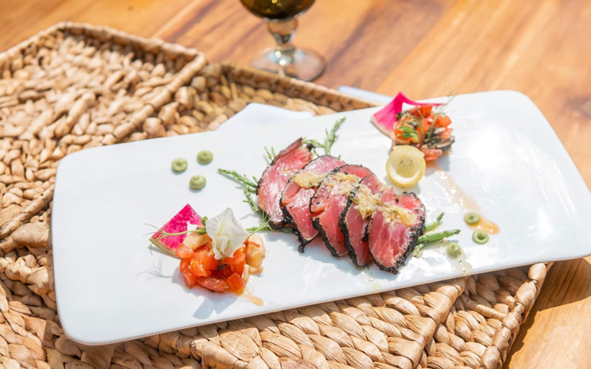 A beautifully plated dish featuring seared tuna slices with garnishes and a side of fresh salsa, served on a woven mat.