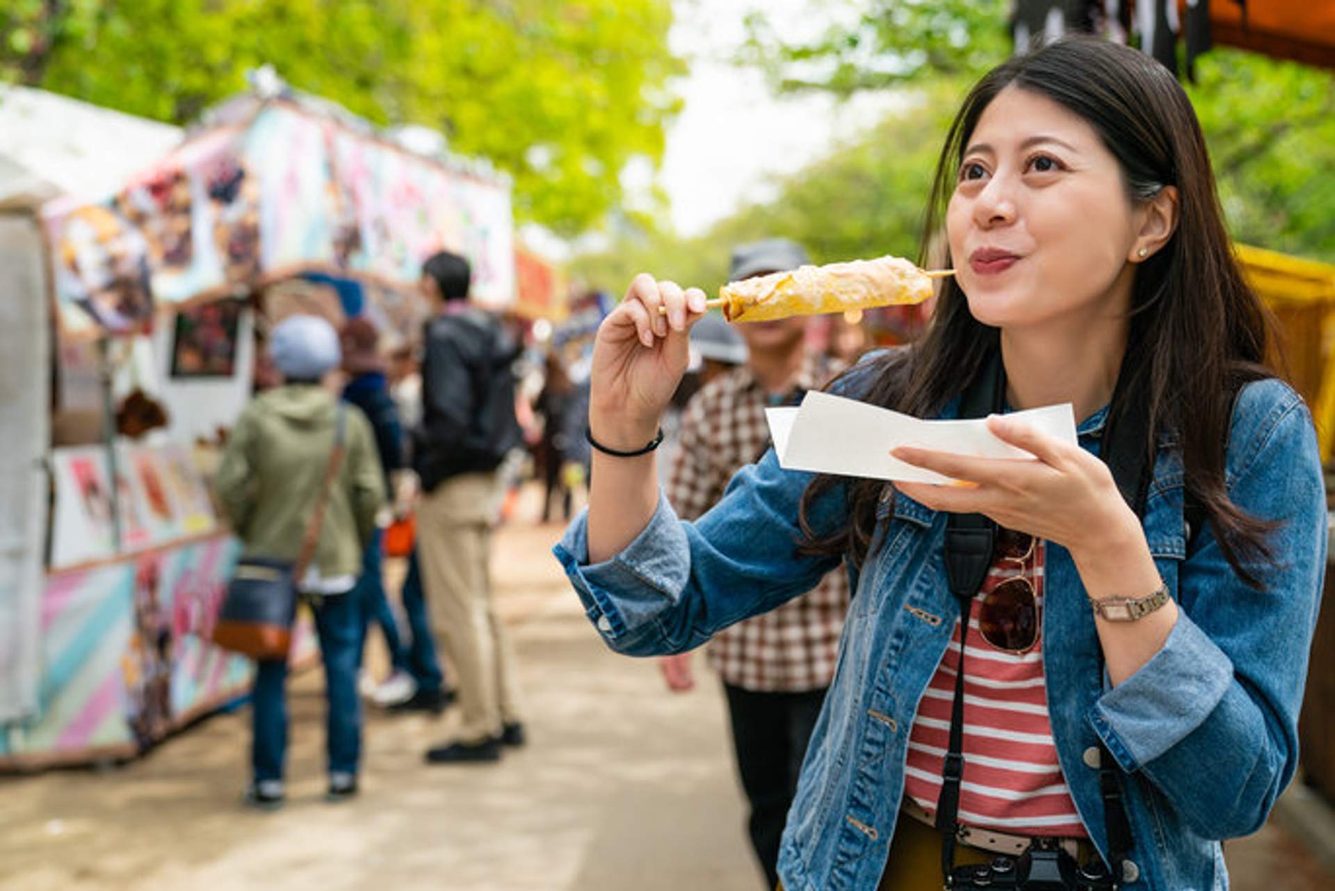 Una mujer disfruta comiendo elote, un antojito mexicano, en un mercado al aire libre.