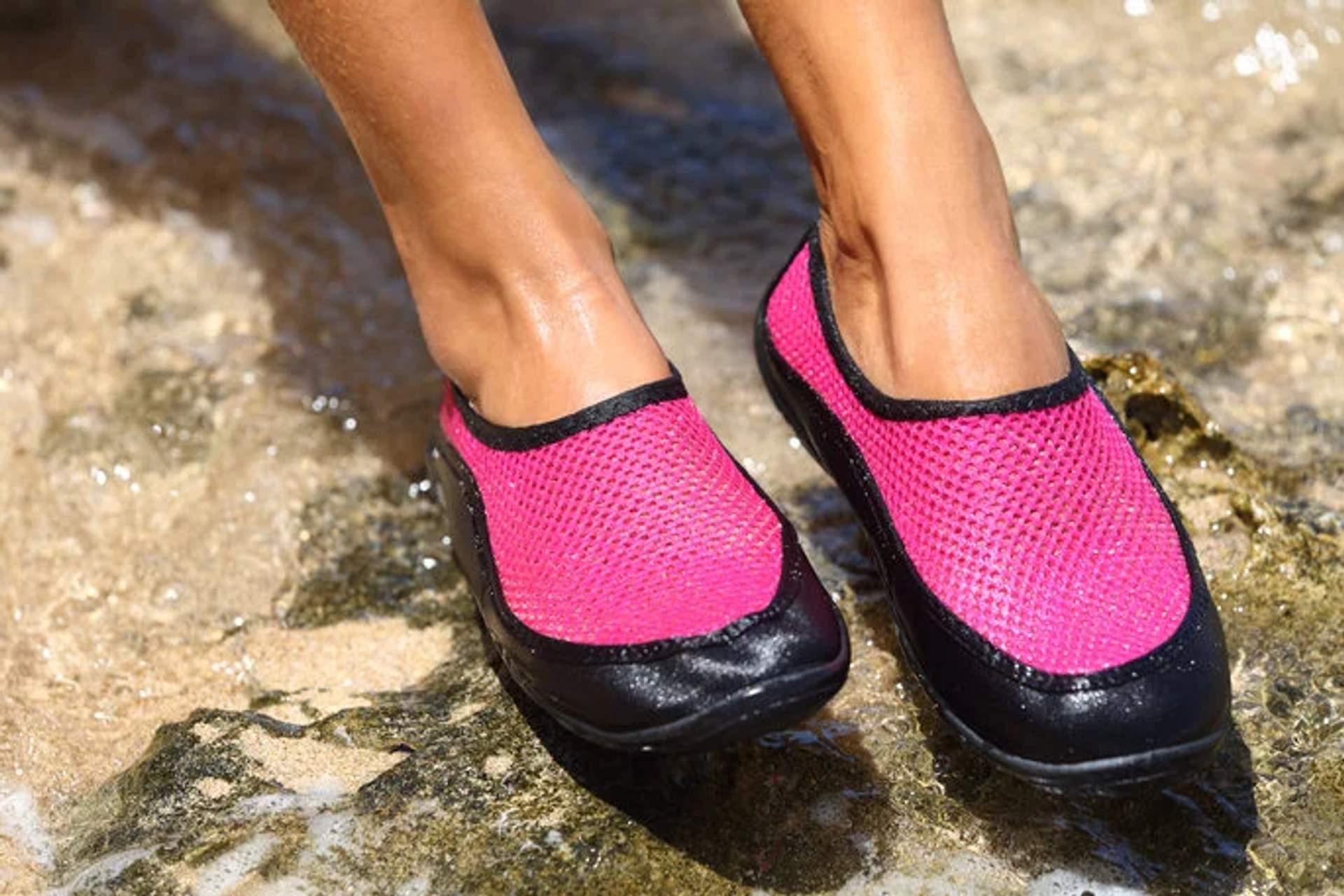 Close-up of feet wearing pink and black water shoes on a rocky beach.