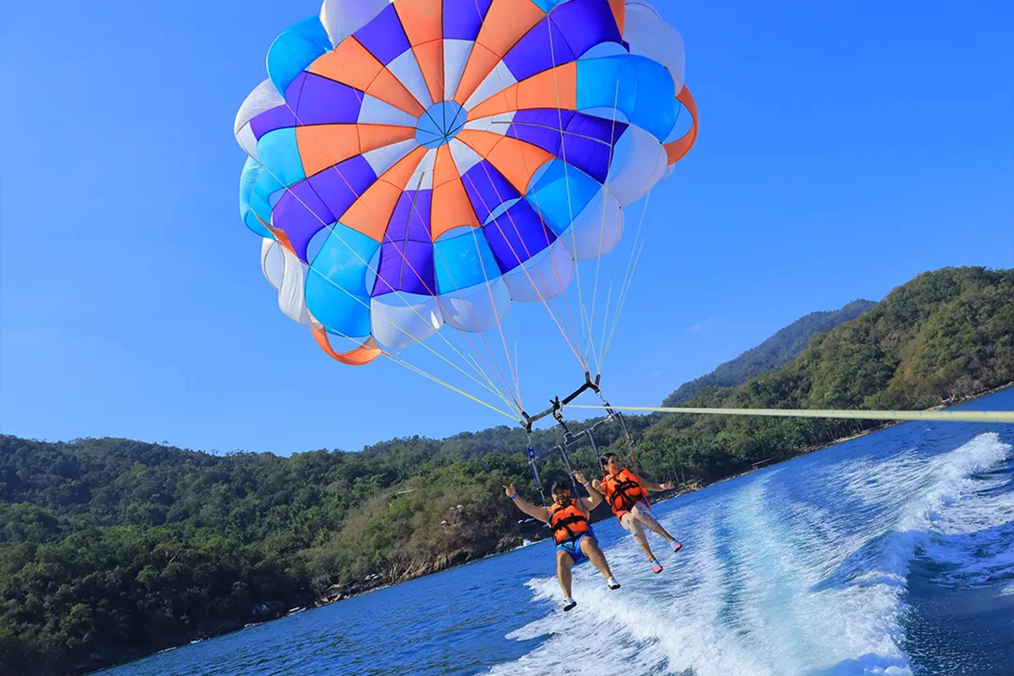 Aventura de parasailing sobre las aguas azules de Puerto Vallarta con montañas verdes al fondo.