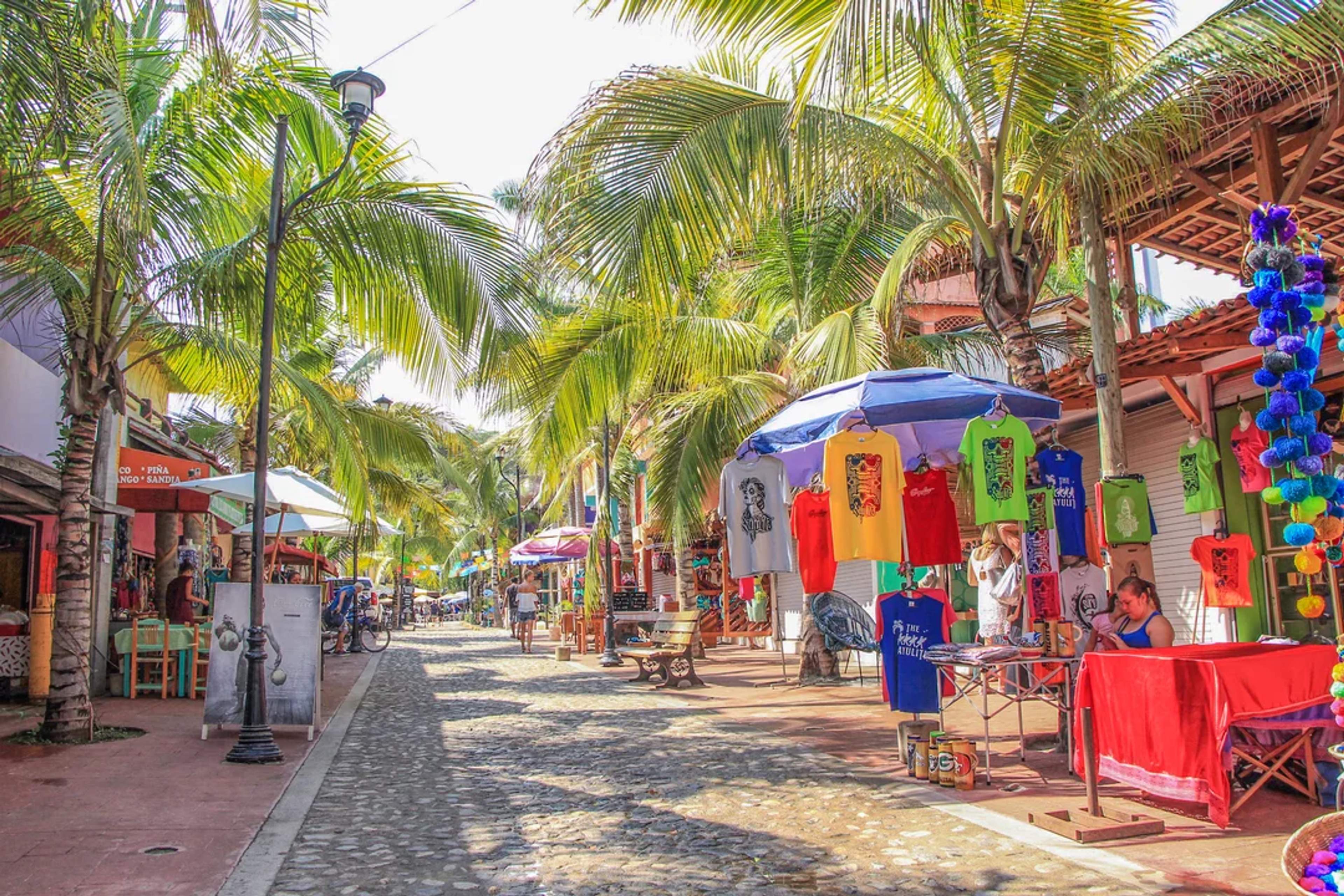 Colorful street market in Sayulita with palm trees, t-shirts, and local vendors under the sun.