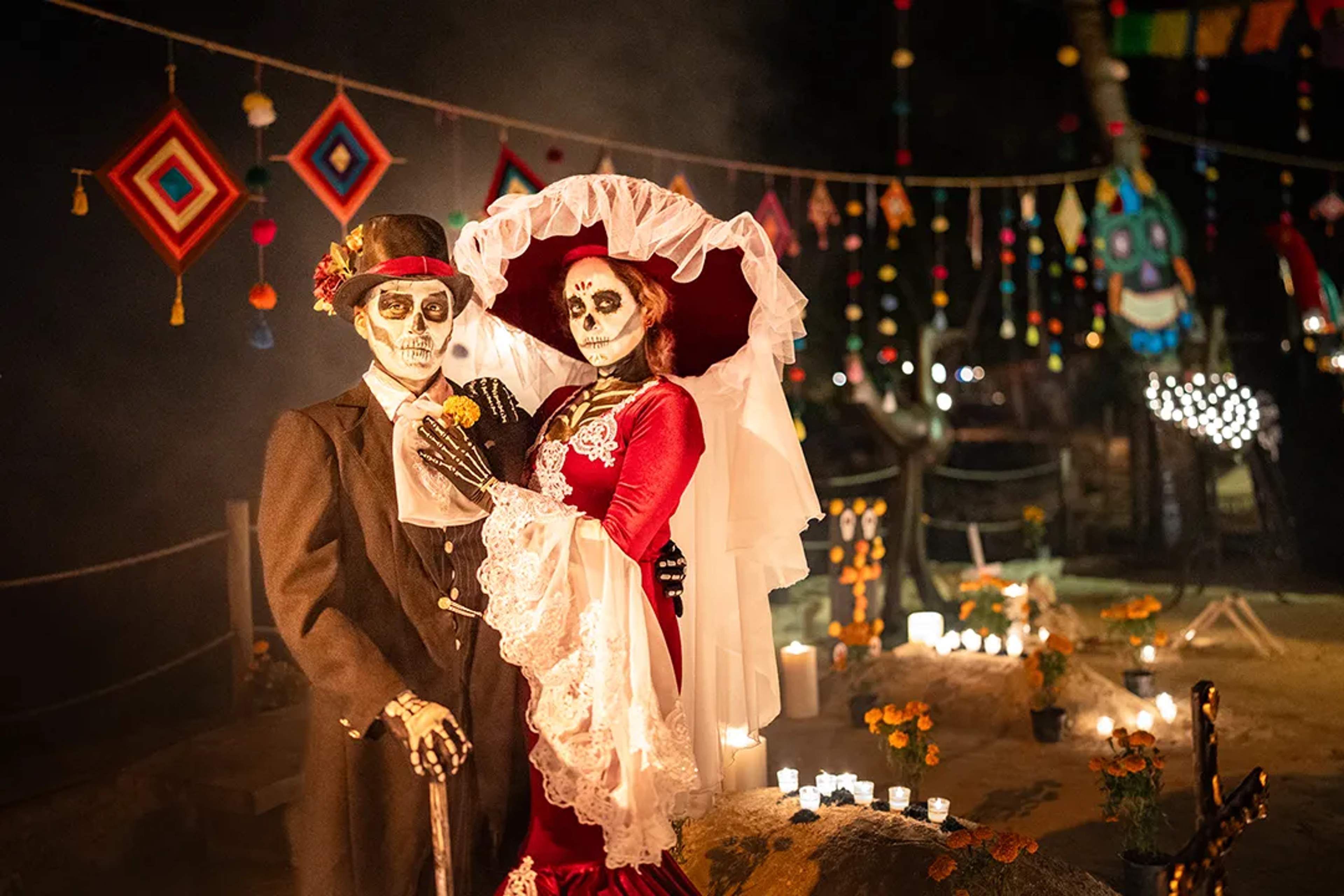 Pareja de Catrina y Catrín en celebración de Día de Muertos con velas y cempasúchil por la noche