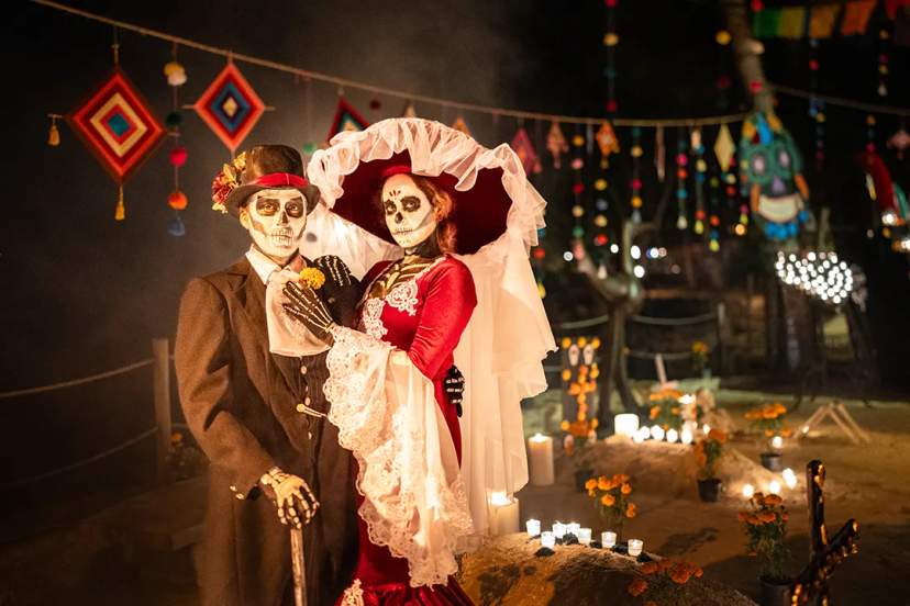 Catrina and Catrín couple in traditional Day of the Dead celebration with candles and marigolds at night