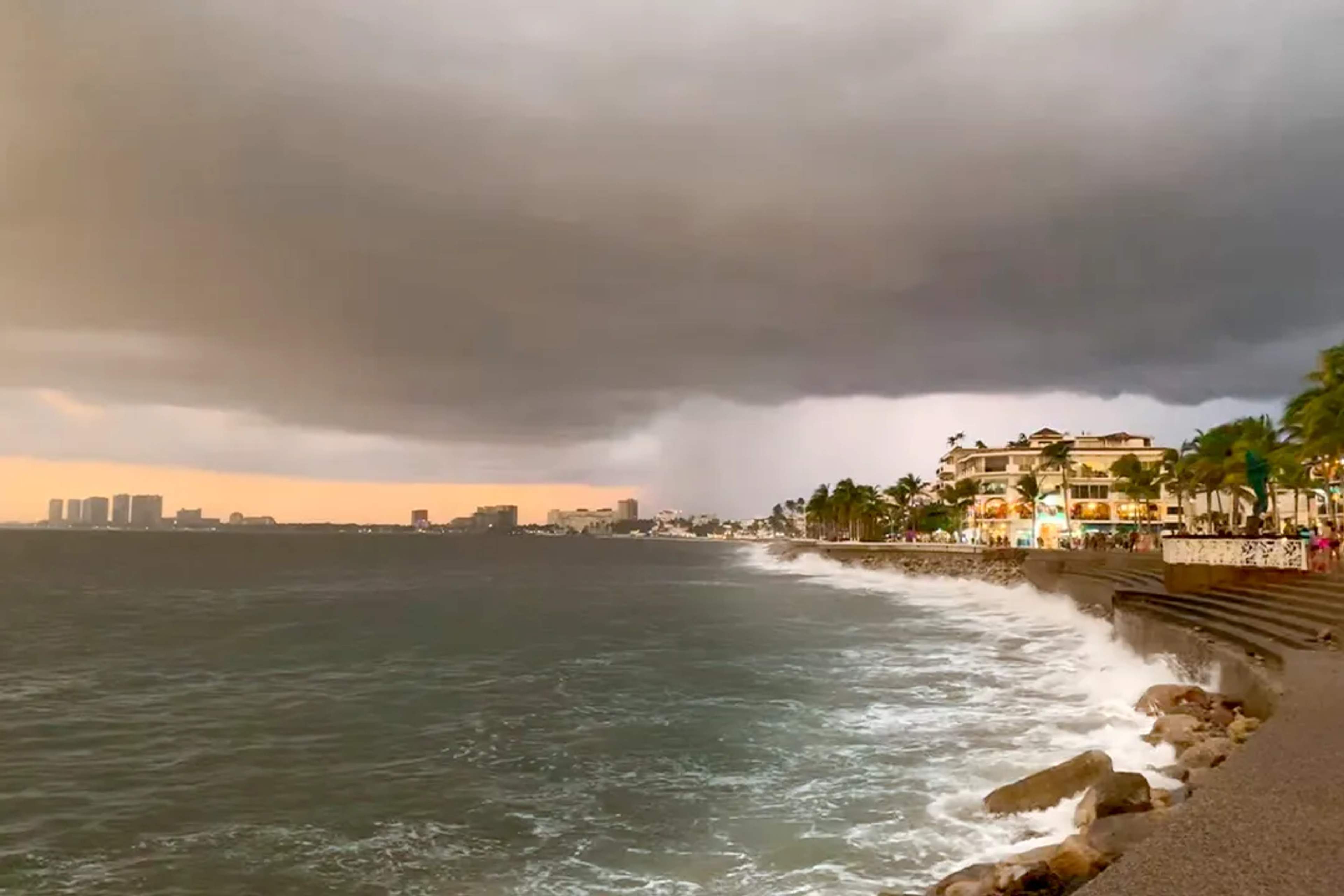 Nubes de tormenta cubren el Malecón de Vallarta mientras las olas chocan y las luces brillan.