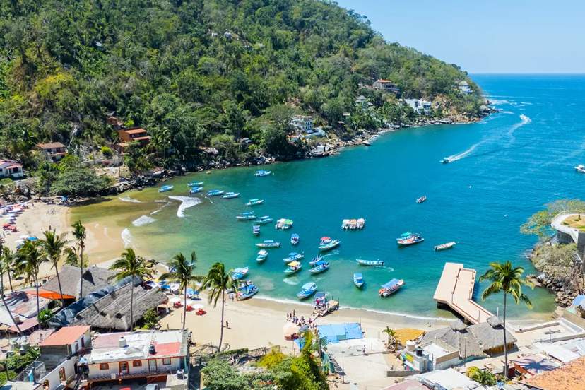 Aerial view of Boca de Tomatlán, with fishing boats anchored in turquoise waters by the beach.