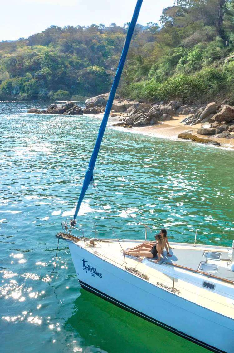 A sailboat anchored on the south shore of Puerto Vallarta with lush greenery and calm waters.