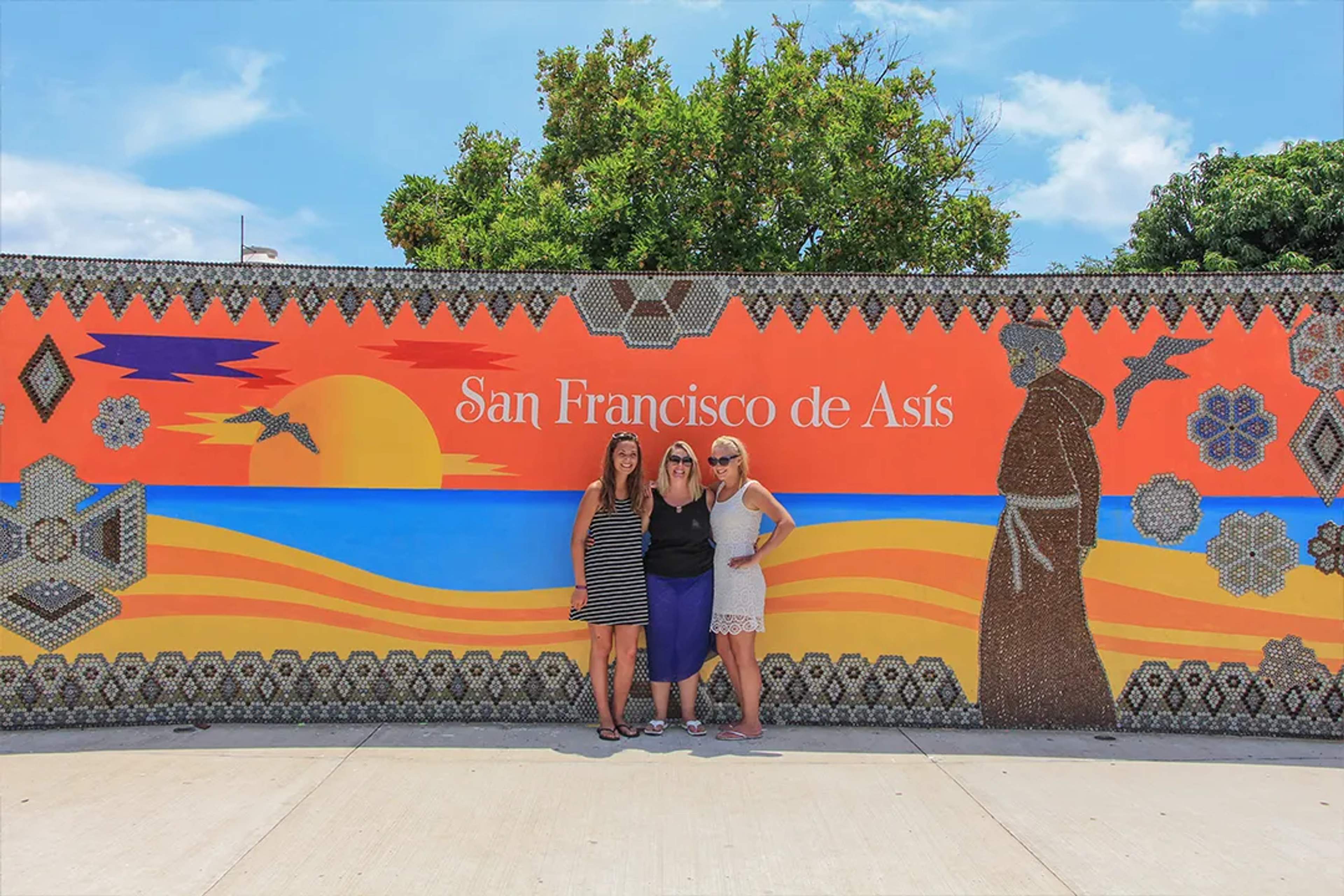 Visitors posing by the San Francisco de Asís mural in Sayulita, colorful mosaic artwork and coastal sunset design