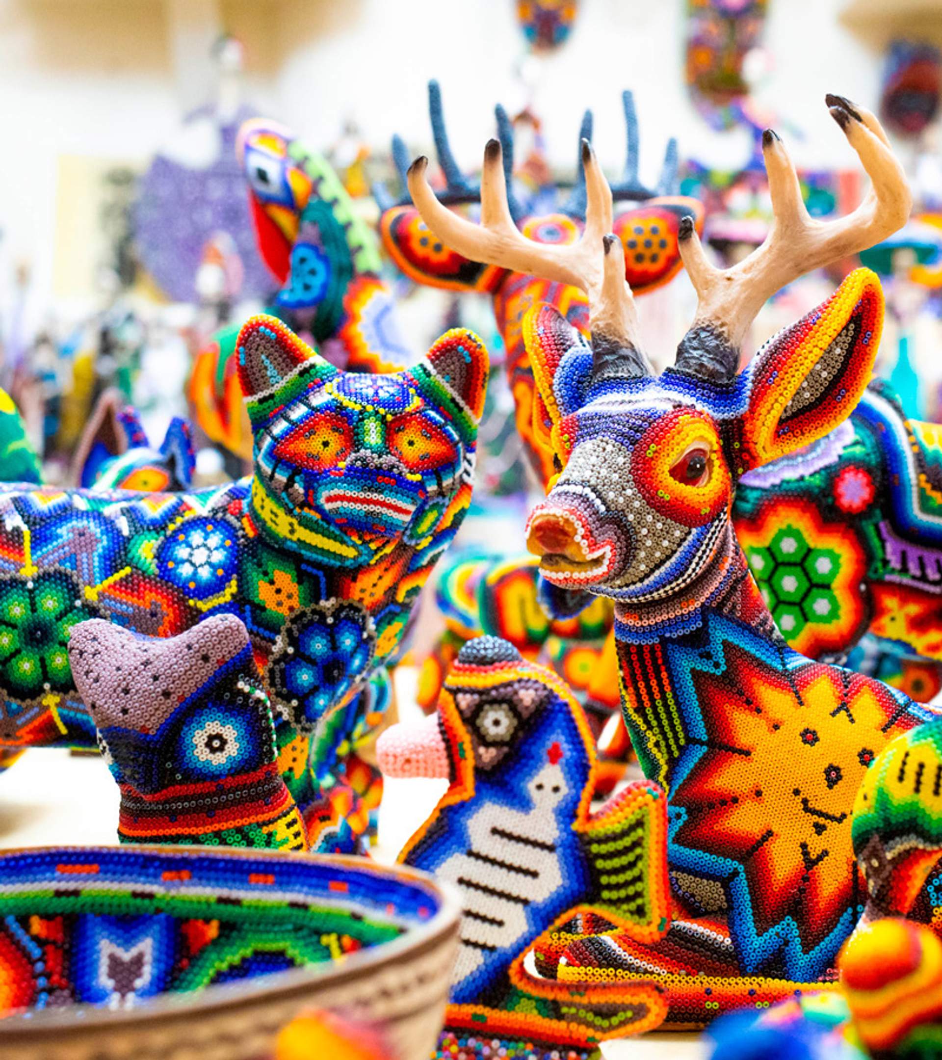 Esculturas hechas a mano con cuentas coloridas, incluyendo un gato, un venado y otros animales, exhibidas en un puesto de mercado. Los diseños intrincados y los colores vibrantes muestran la artesanía tradicional.