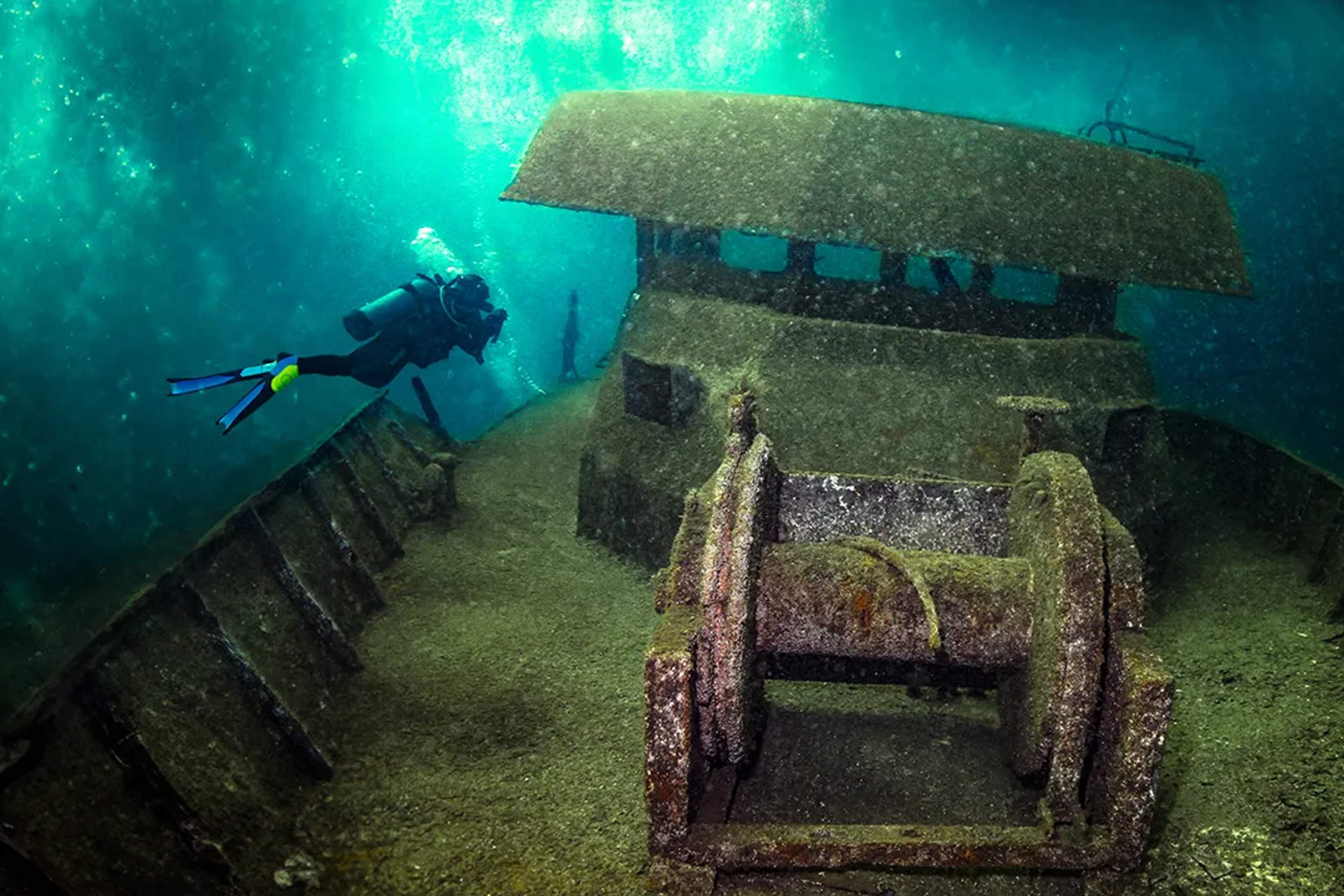 Scuba diver explores the sunken shipwreck of the Princesa Wreck, its rusty structure resting on the ocean floor.