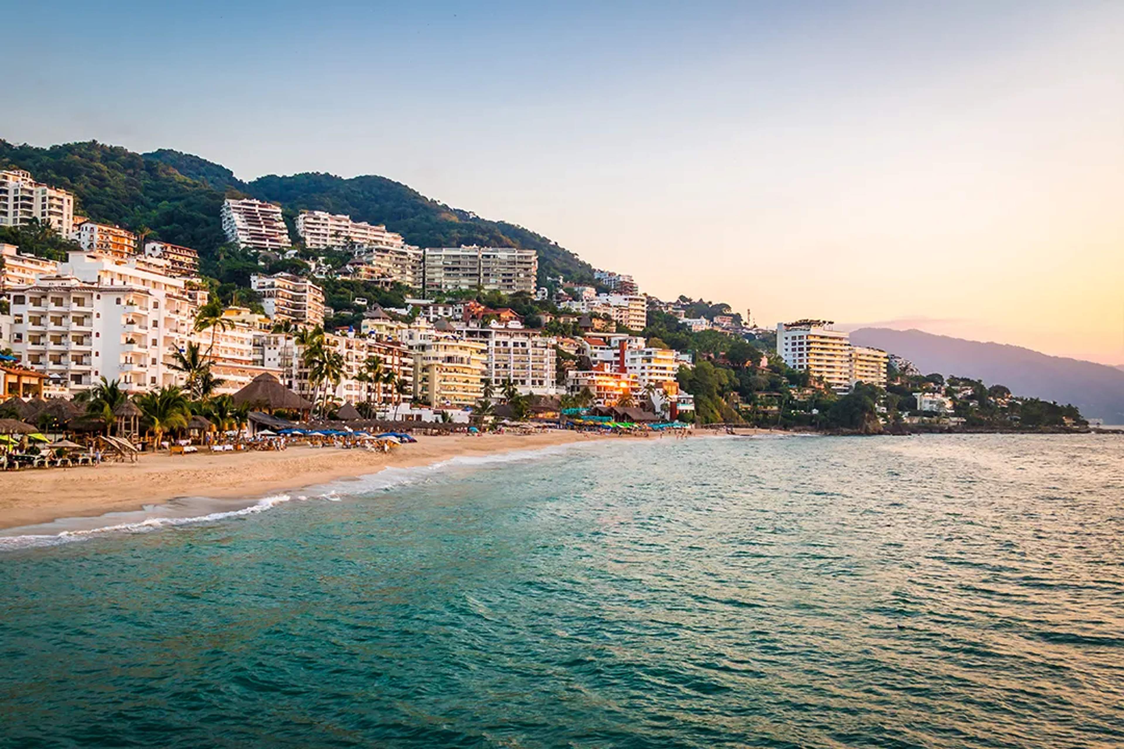 Atardecer en la Zona Romántica de Vallarta, con luz dorada sobre la playa y las colinas.